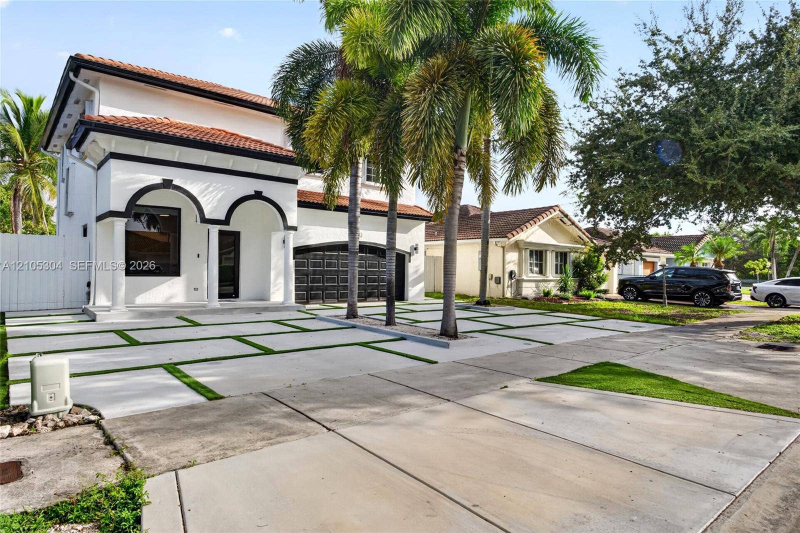 15217 SW 36th Terrace, Miami, FL 33185 Two-story stucco exterior featuring arched entryways, a tiled roof, multi-car garage, and a concrete paver driveway with integrated green space
