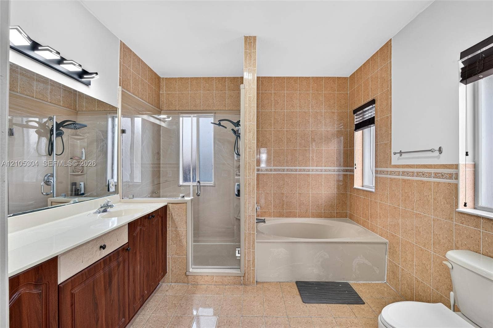 15217 SW 36th Terrace, Miami, FL 33185 Bathroom featuring a dual-sink wood-finish vanity with an integrated countertop, a glass-enclosed shower, a deep soaking tub, and tile wall surrounds