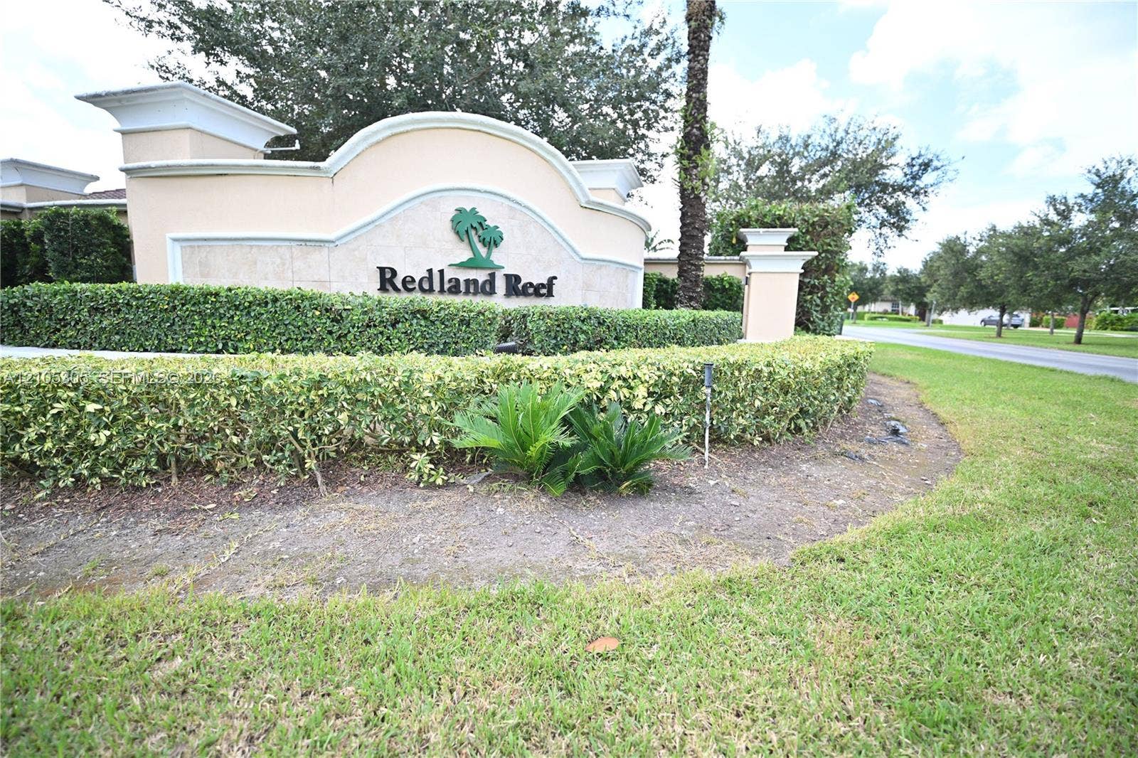 Community entrance sign featuring a decorative arch, textured stucco finish, and lush green landscaping