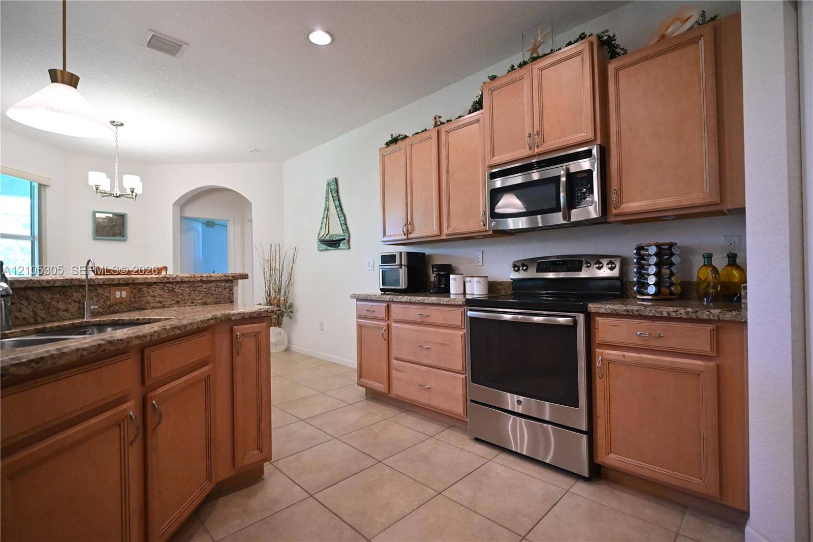 Kitchen featuring a stainless steel range, built-in microwave, wood cabinetry, stone countertops, and tile flooring