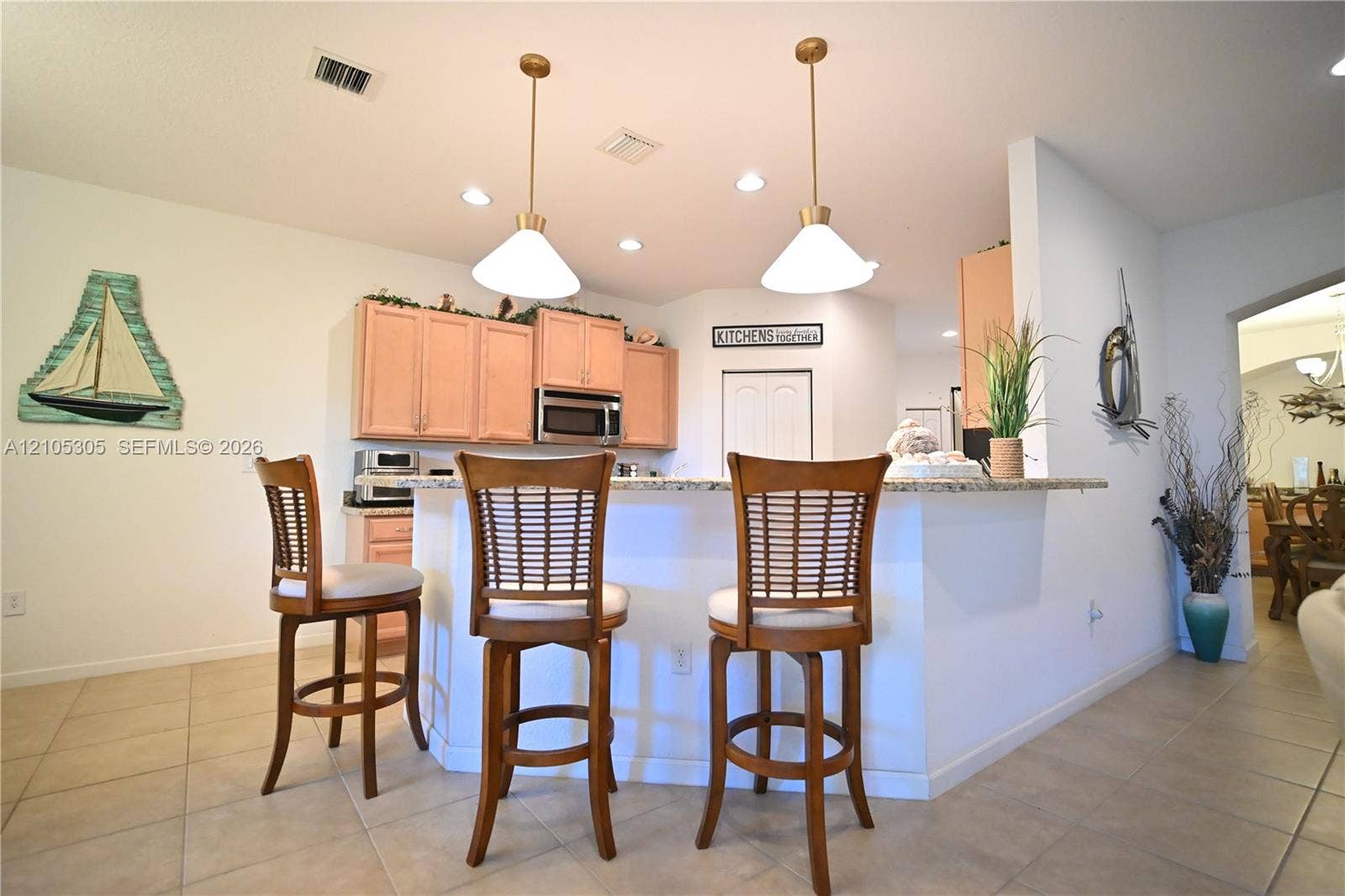 Kitchen with light-toned cabinetry, stainless steel microwave, recessed lighting, and two pendant lights over a countertop bar