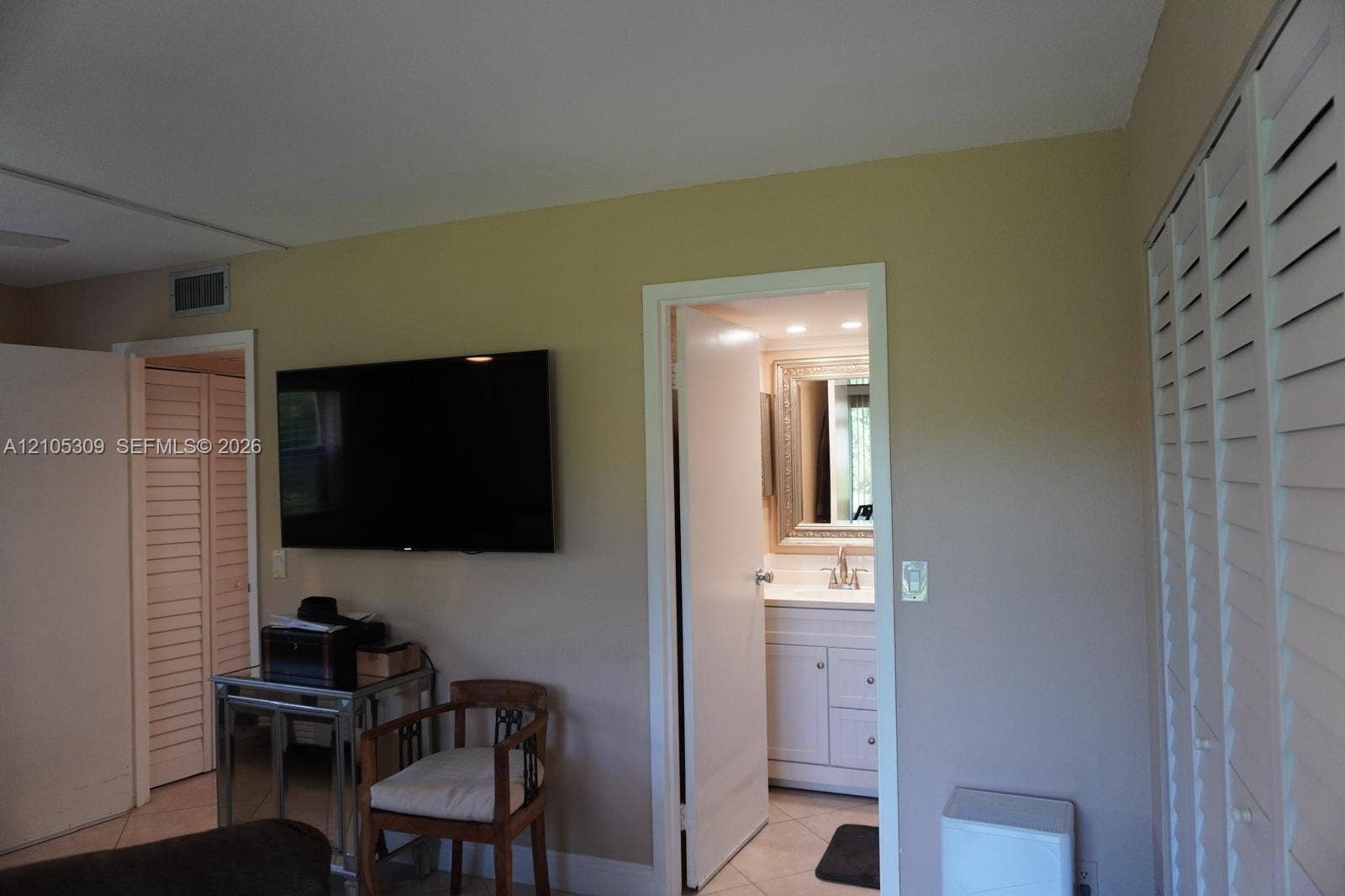 542 Saxony L, #542, Delray Beach, FL 33446 Neutral-toned interior space featuring white louvered closet doors, tiled flooring, and a vanity cabinet with a metallic framed mirror