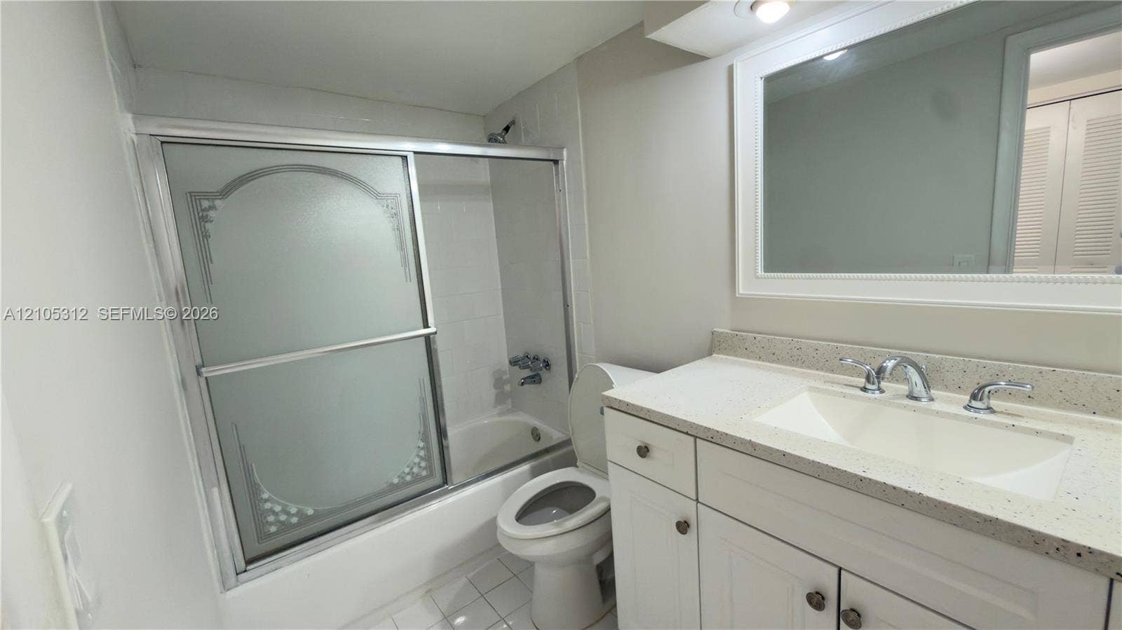 6900 N Kendall Drive, #A304, Pinecrest, Pinecrest, FL 33156 Bathroom featuring a white vanity cabinet with a speckled countertop, integrated sink with a chrome faucet, large framed wall mirror, and a shower-tub combination with sliding etched-glass doors