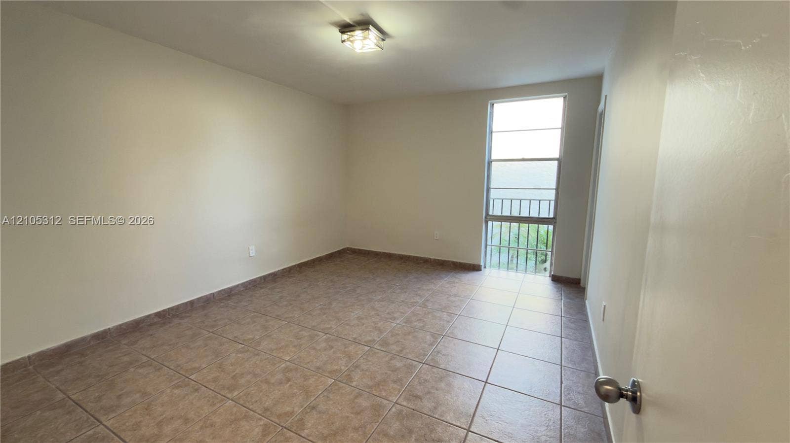 6900 N Kendall Drive, #A304, Pinecrest, Pinecrest, FL 33156 Neutral-toned interior space featuring large-format ceramic tile flooring, a rectangular multi-pane window with a metal security grate, and a square-profile ceiling-mounted light fixture