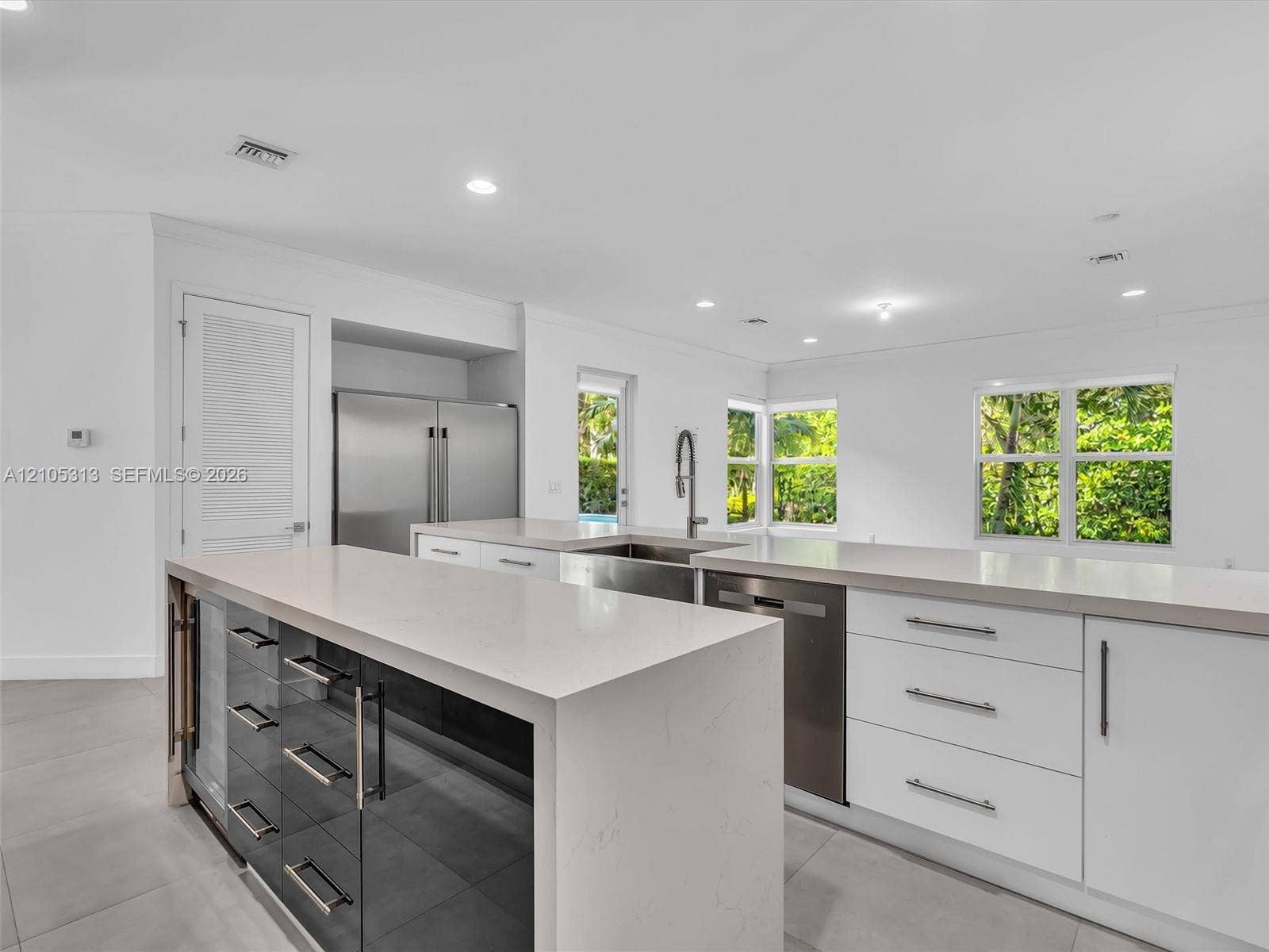 Kitchen featuring a waterfall-edge stone countertop, custom cabinetry with integrated wine refrigeration, stainless steel appliances, and large-format tile flooring