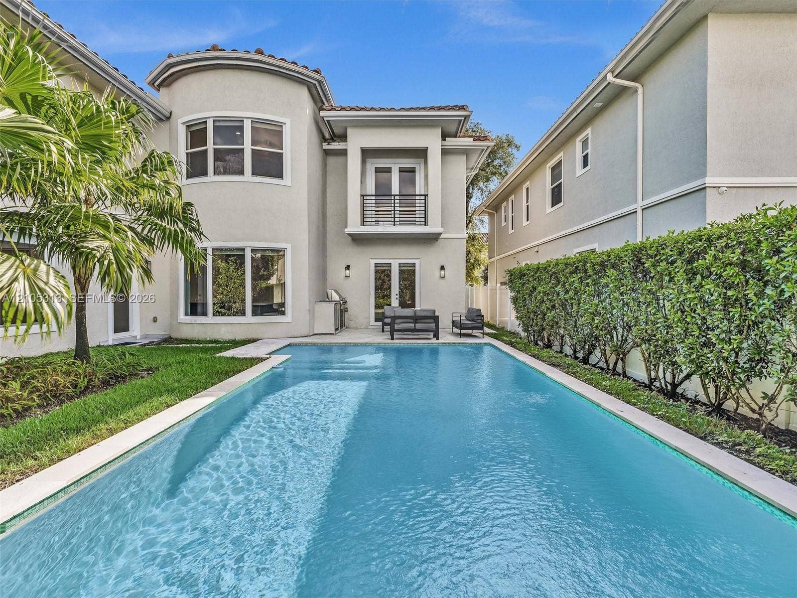 Stucco exterior featuring a second-story balcony with metal railing, a private swimming pool with integrated tanning ledge, and a rear patio area
