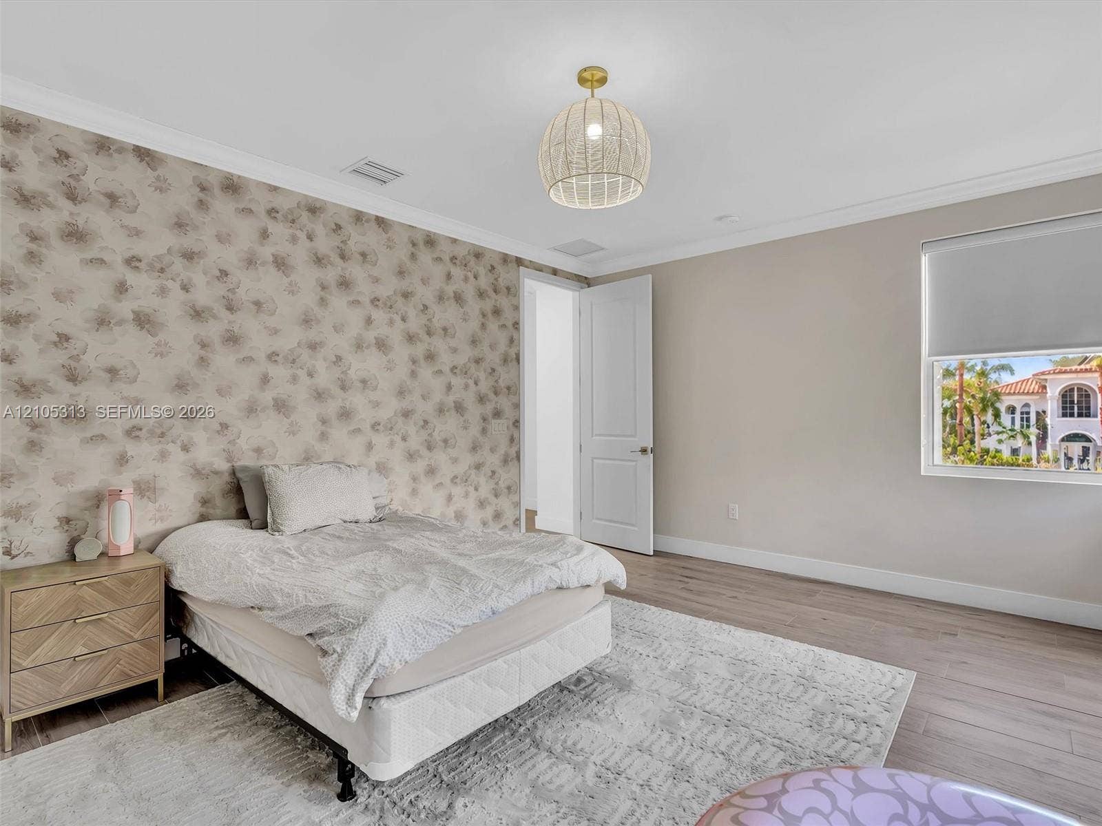 Interior space featuring wood-finish flooring, a decorative patterned accent wall, crown molding, and a drum-style pendant light fixture