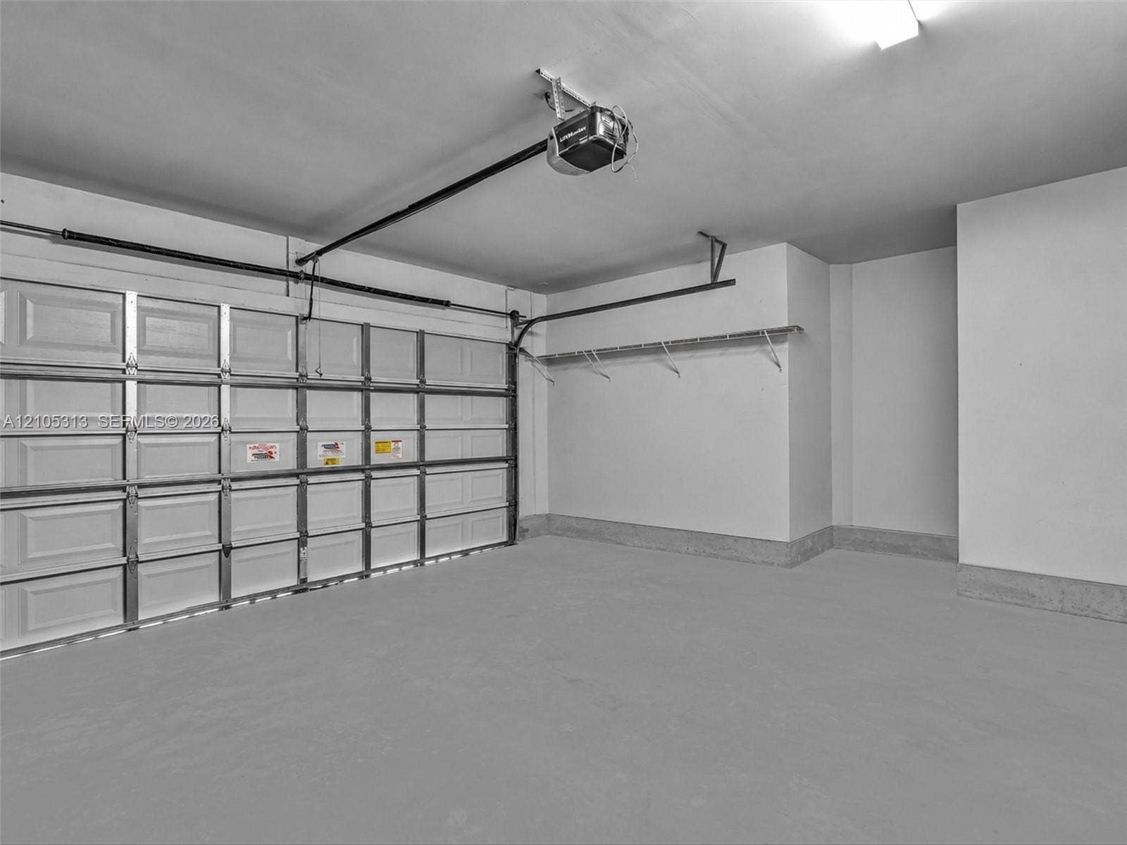 Two-car garage featuring a sectional door, concrete flooring, automatic door opener, and wall-mounted shelving