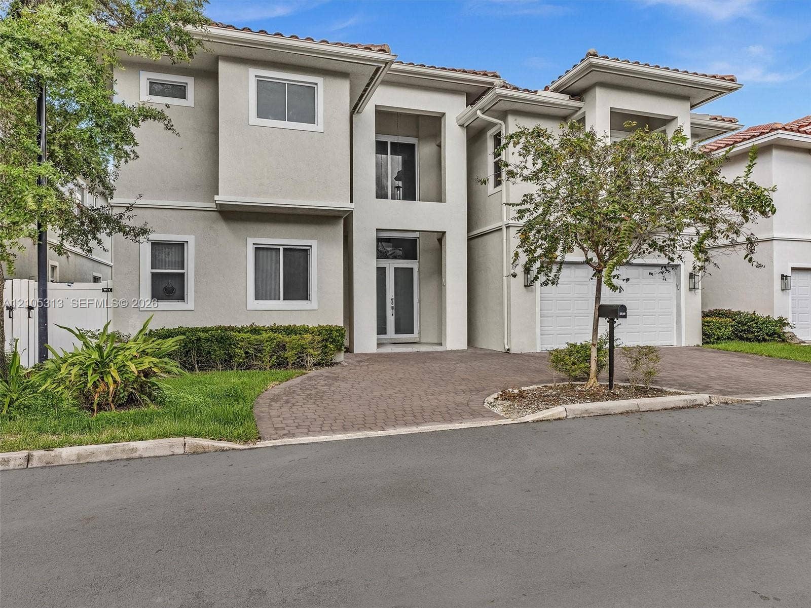 Two-story residence featuring a tile roof, stucco exterior, paver driveway, covered entryway, and an attached two-car garage