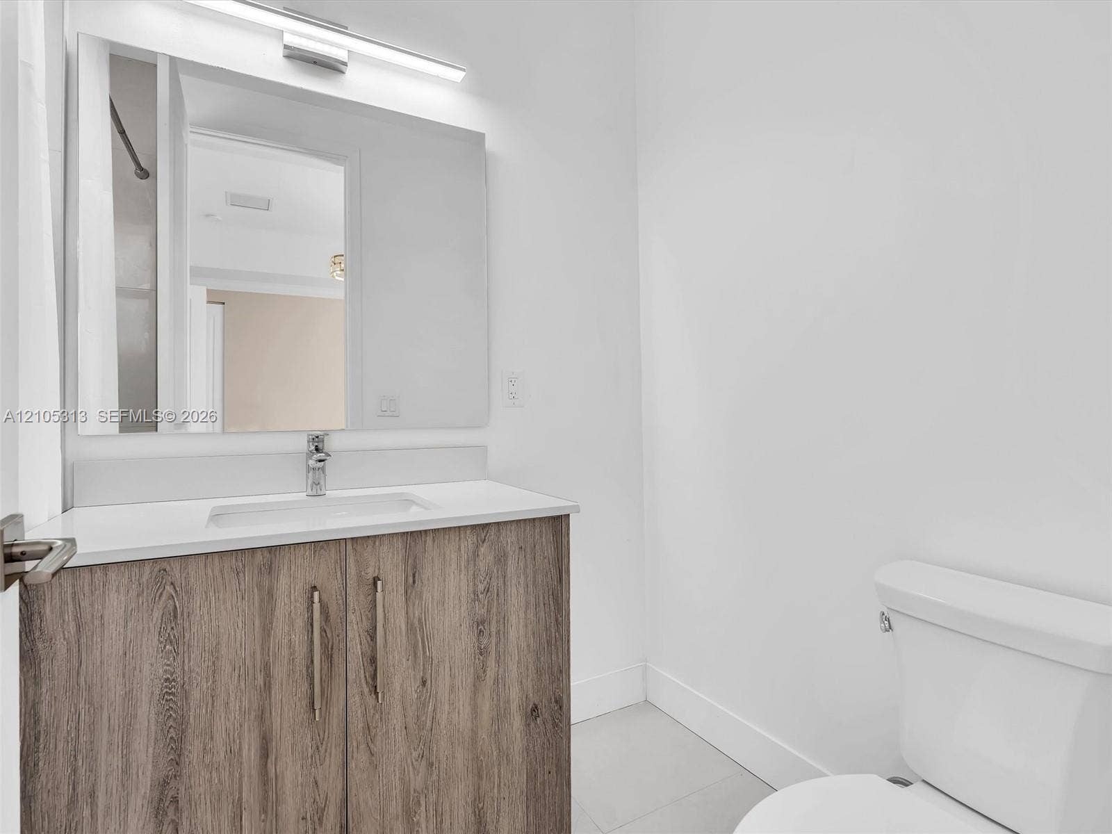 Bathroom featuring a wood-finish vanity with a stone-composite countertop, undermount sink, linear wall-mounted lighting, and a large frameless mirror