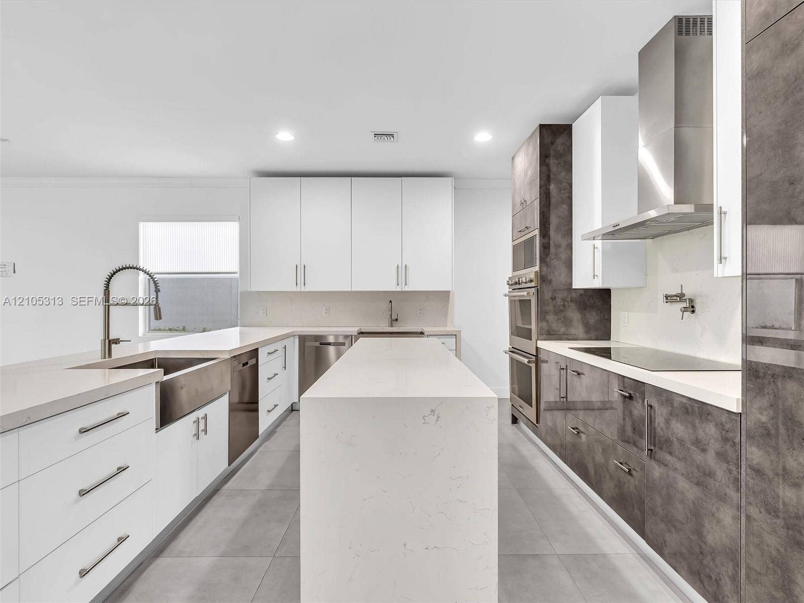 Kitchen featuring a central island with a quartz countertop, flat-panel cabinetry, stainless steel appliances, a farmhouse sink, and a wall-mounted pot filler