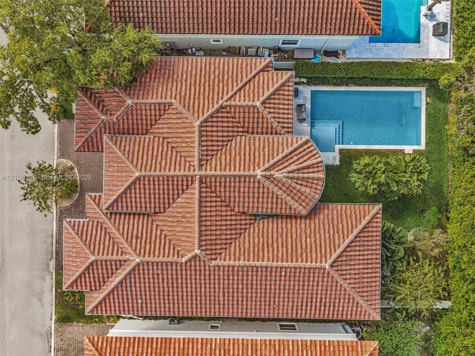 Aerial view featuring a multi-gabled clay tile roof, a rectangular swimming pool, and landscaped perimeter greenery