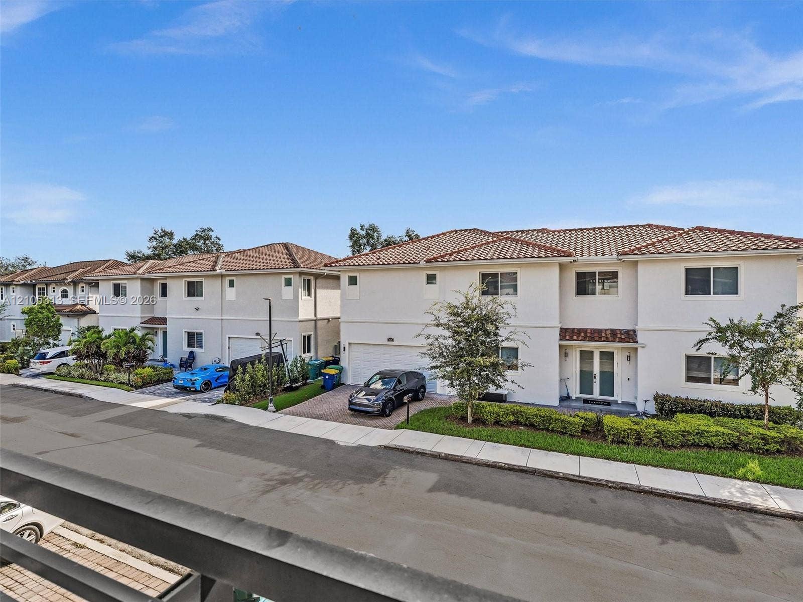Two-story exterior featuring light-toned stucco siding, a tiled roof, paver driveways, and integrated garage doors