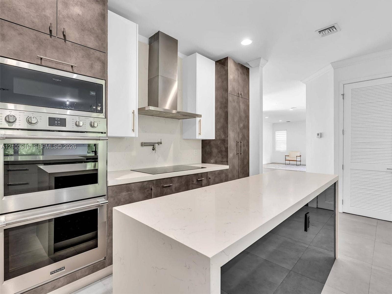 Contemporary kitchen featuring two-tone cabinetry, quartz waterfall island, stainless steel wall-mounted oven, and a professional-grade range hood