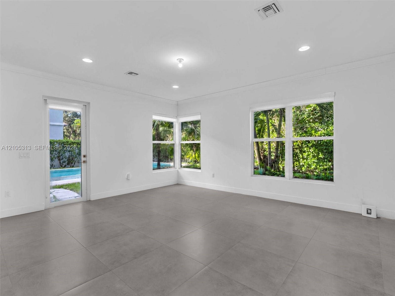 Interior space featuring large-format grey tile flooring, recessed ceiling lighting, multiple dual-pane windows, and a glass-paneled exterior door