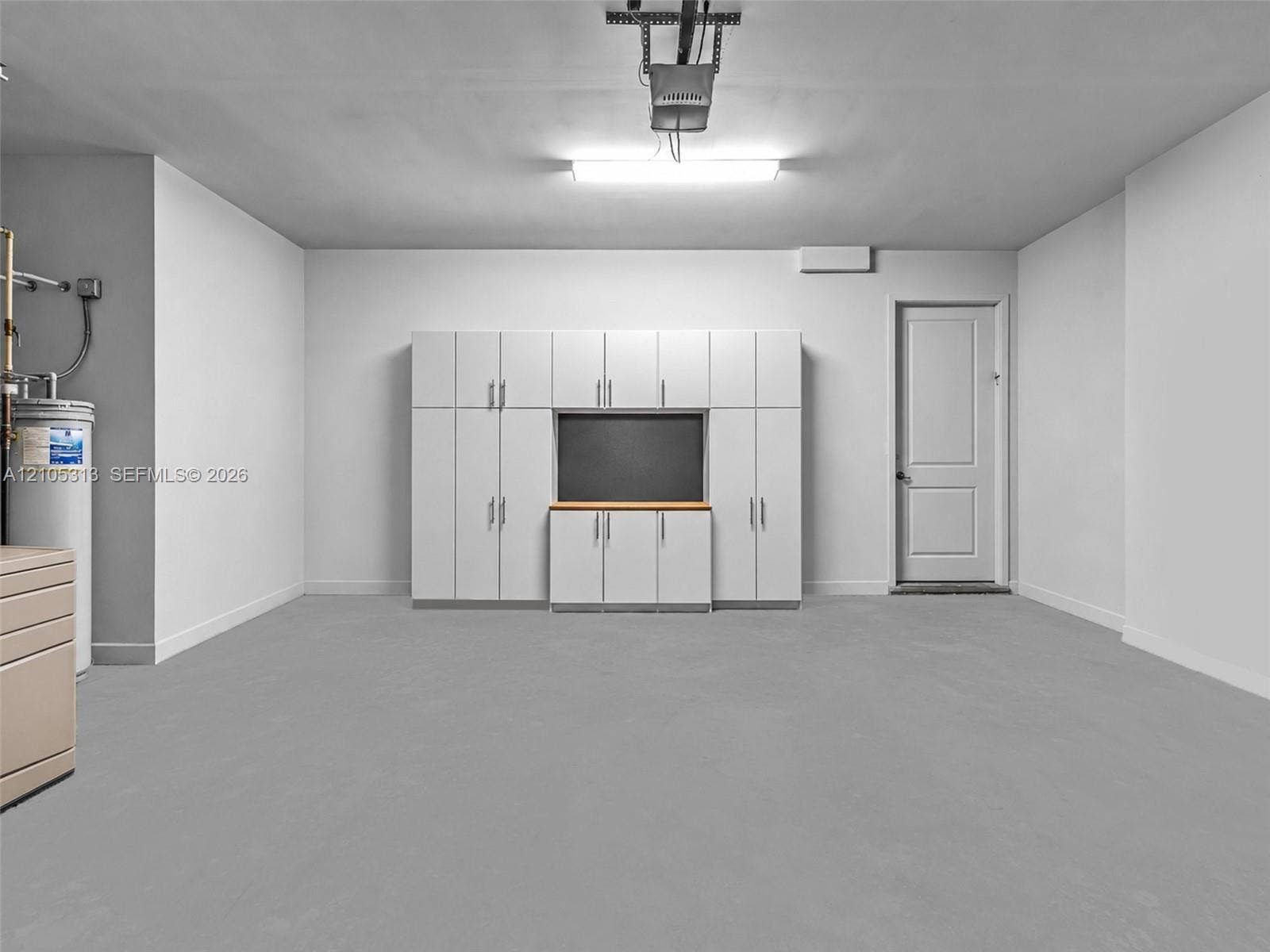Garage featuring white built-in cabinetry with a dedicated workspace, smooth concrete flooring, and a single-panel interior door