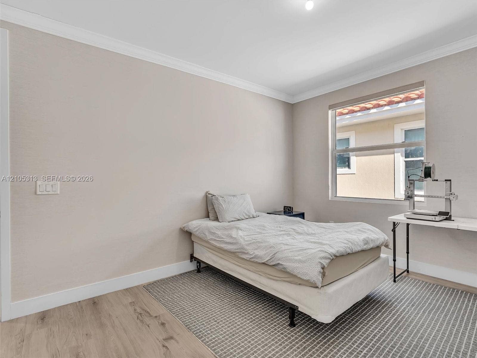 Neutral-toned interior featuring wood-finish flooring, crown molding, and a single-pane window