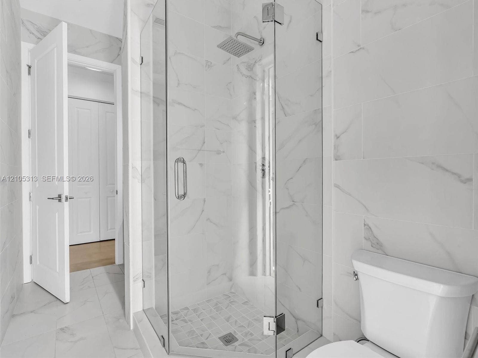Walk-in shower featuring a frameless glass enclosure, rain-style showerhead, large-format stone-finish tile surround, and mosaic tile shower floor