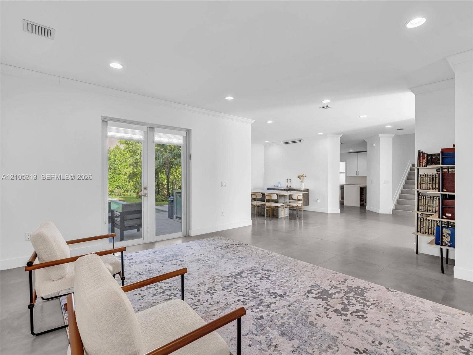 Open-concept interior featuring large-format tile flooring, recessed lighting, white walls, and glass French doors leading to an exterior patio