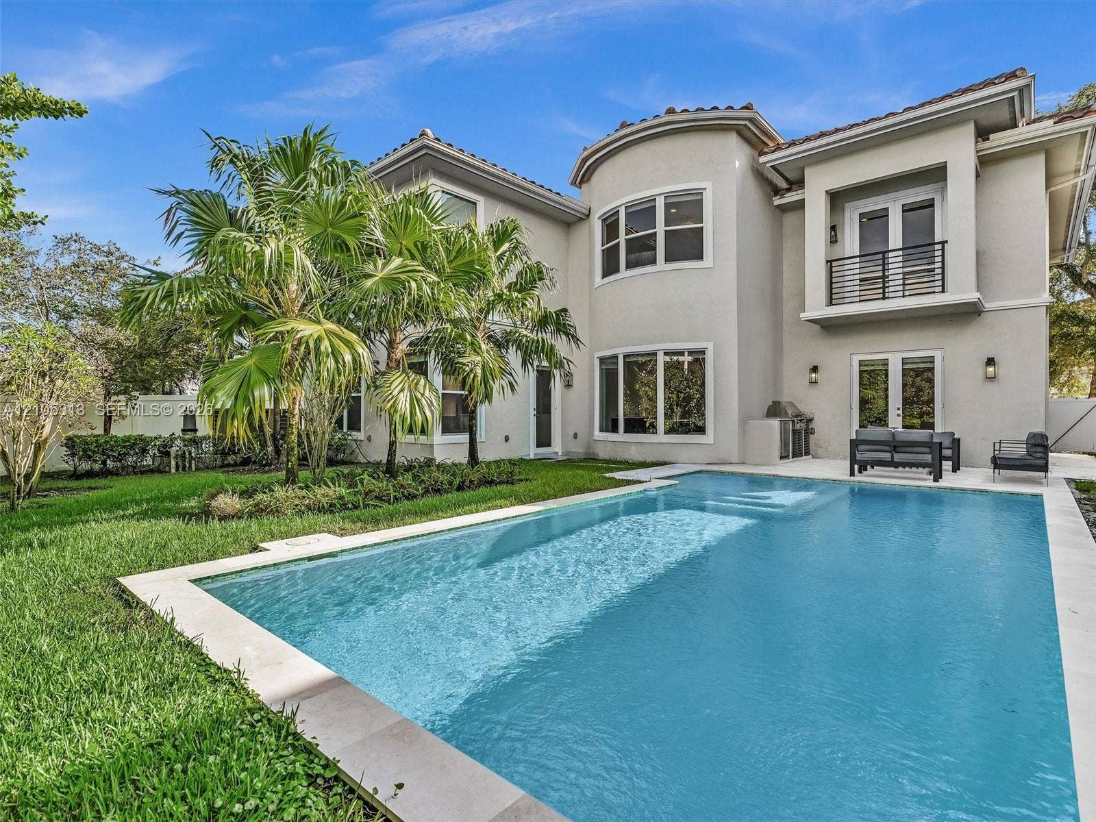 Two-story residence featuring a private swimming pool with stone-tile surround, second-floor balcony with metal railing, stucco exterior, and manicured landscaping