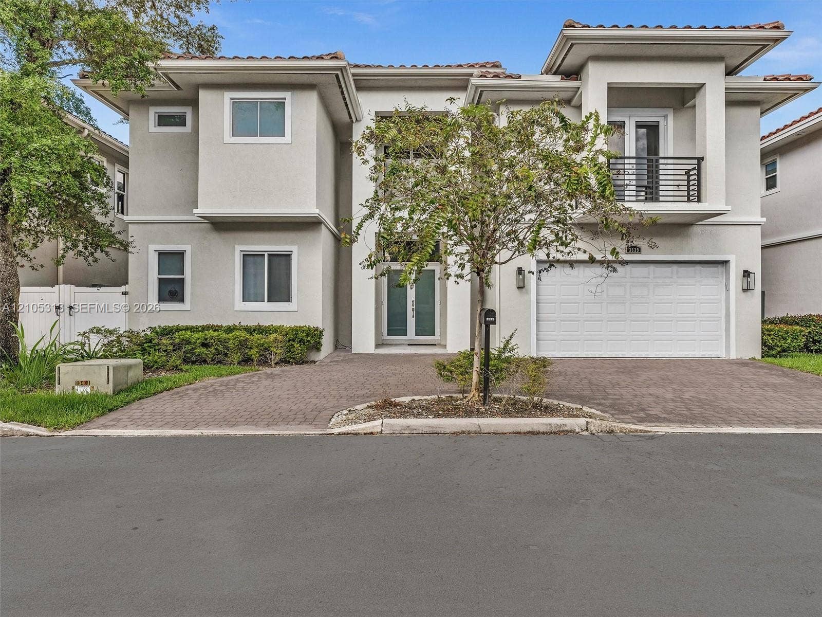 Two-story stucco exterior featuring a paved driveway, integrated two-car garage, upper-level balcony with metal railing, and double-entry doors