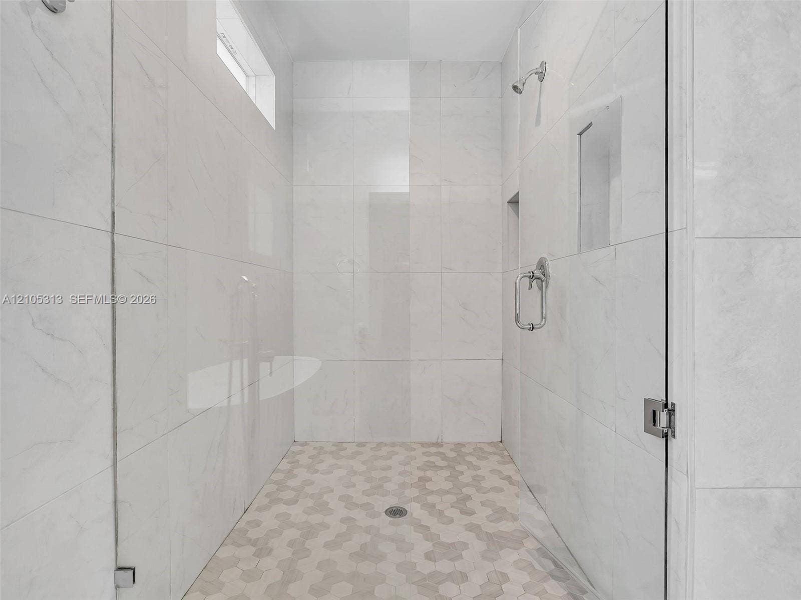 Walk-in shower featuring floor-to-ceiling large-format tile surround, hexagonal tile flooring, frameless glass enclosure, built-in recessed wall niche, and polished chrome hardware