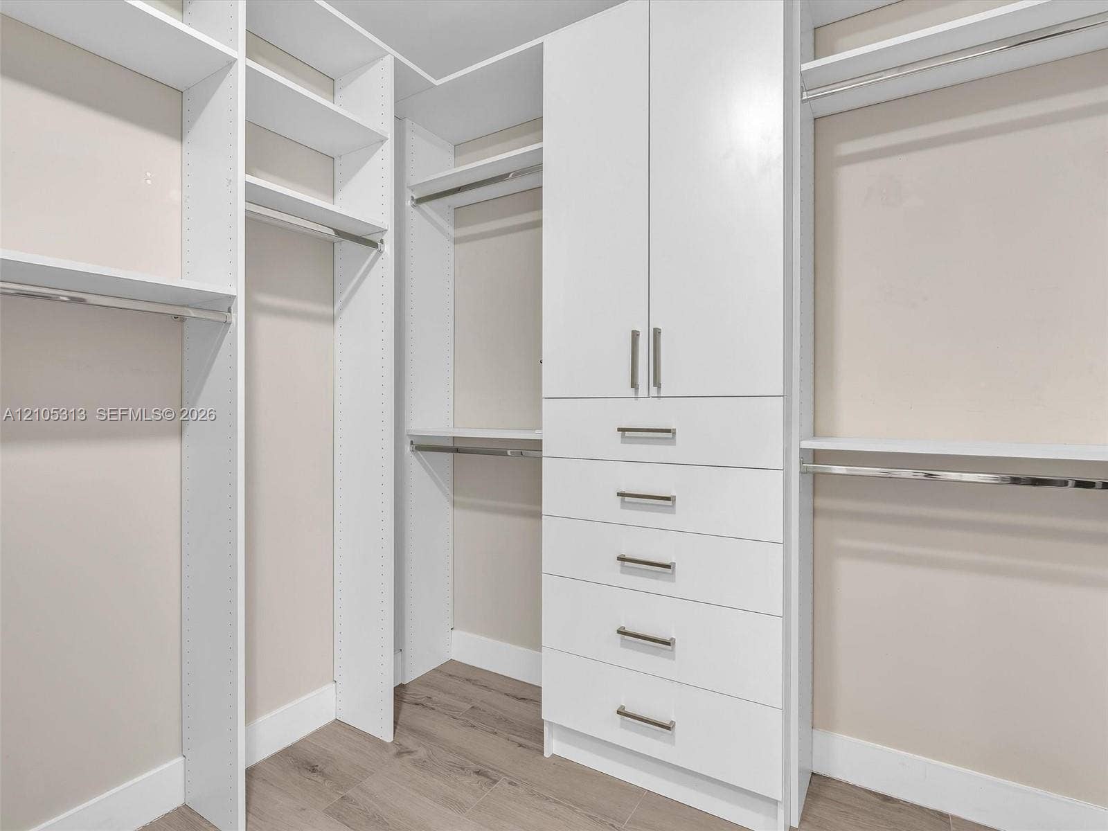 Custom reach-in closet featuring white built-in cabinetry, multiple adjustable shelves, integrated clothing rods, stacked soft-close drawers, and wood-finish flooring