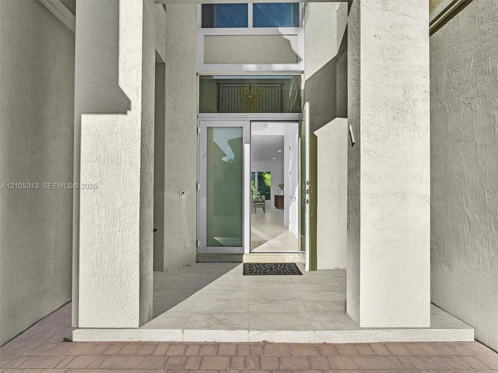 Covered entryway featuring dual structural columns, stone-finish porch flooring, and a multi-pane glass door with a transom window