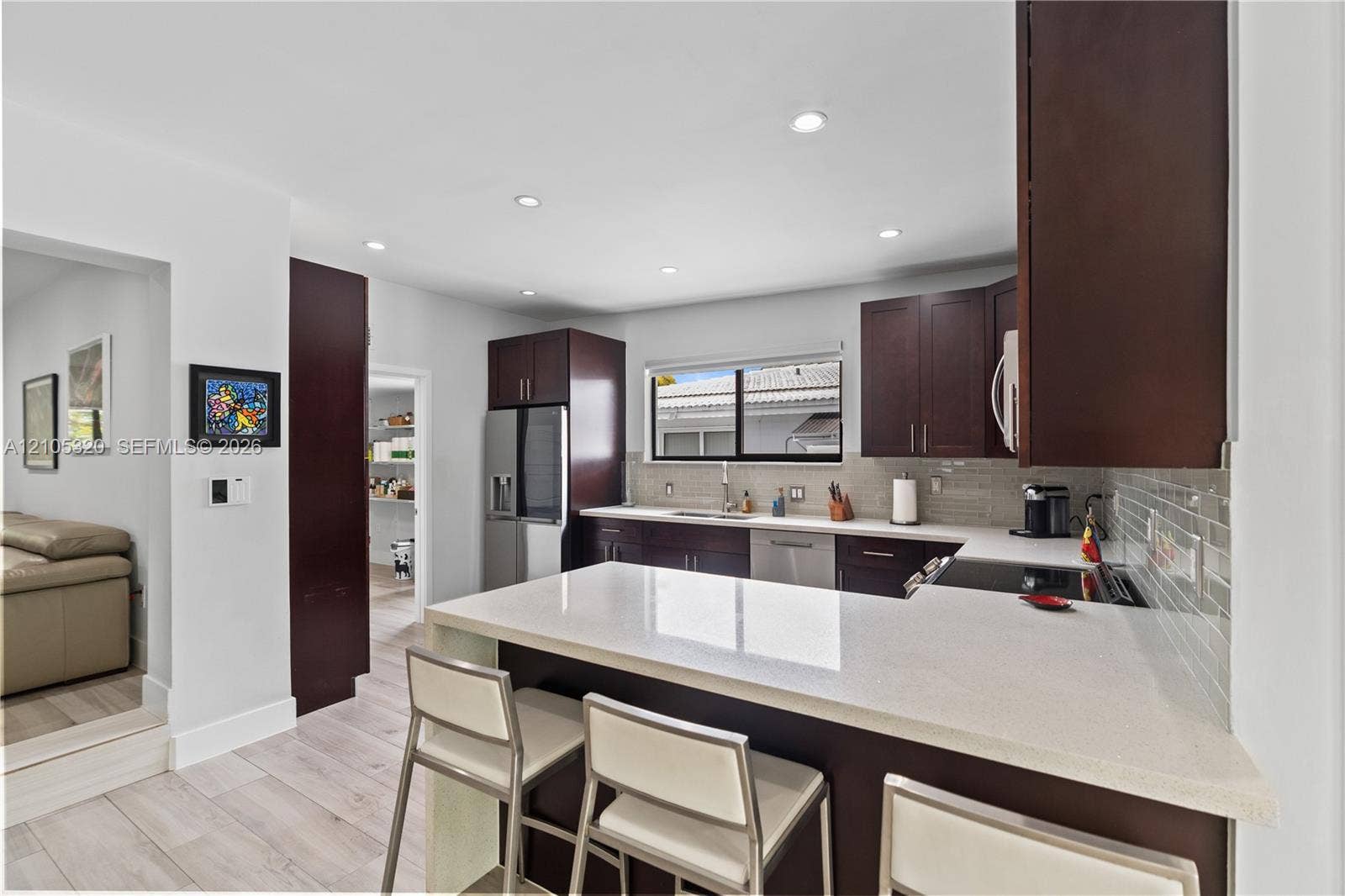Modern kitchen featuring dark wood cabinetry, stainless steel appliances, a white stone countertop, a tile backsplash, and recessed lighting