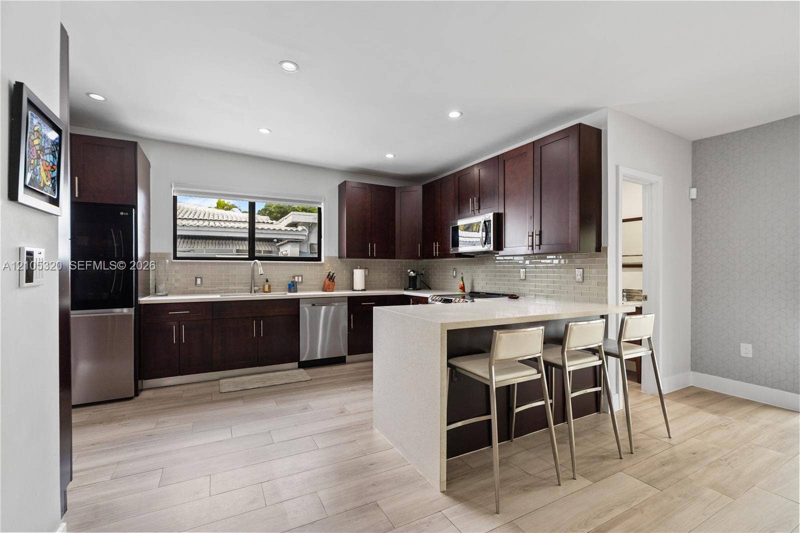 Modern kitchen with wood-finish flooring, dark wood cabinetry, white countertops, and stainless steel appliances