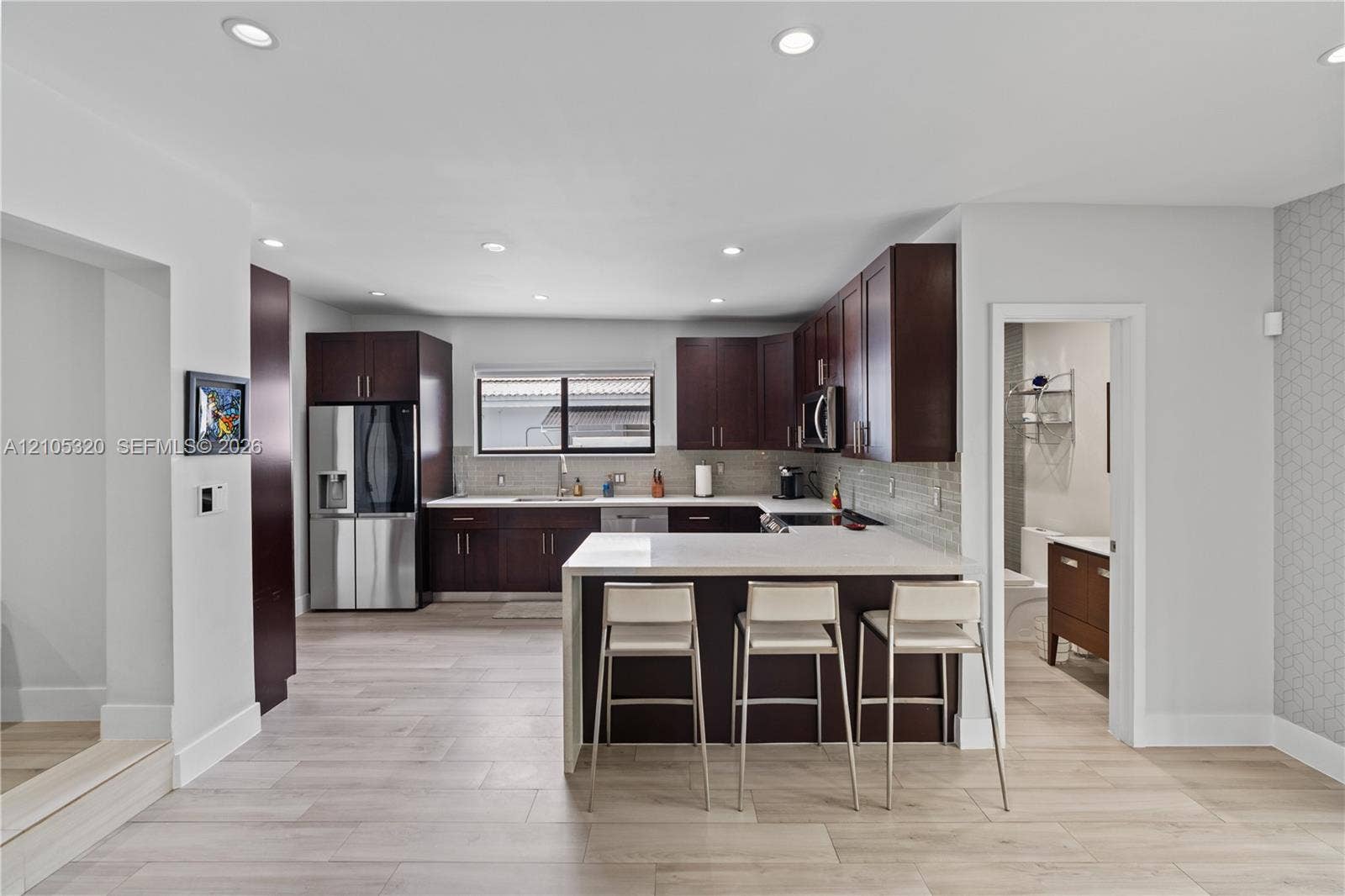 Contemporary kitchen featuring dark wood cabinetry, stainless steel appliances, light countertops, and a full-height tile backsplash