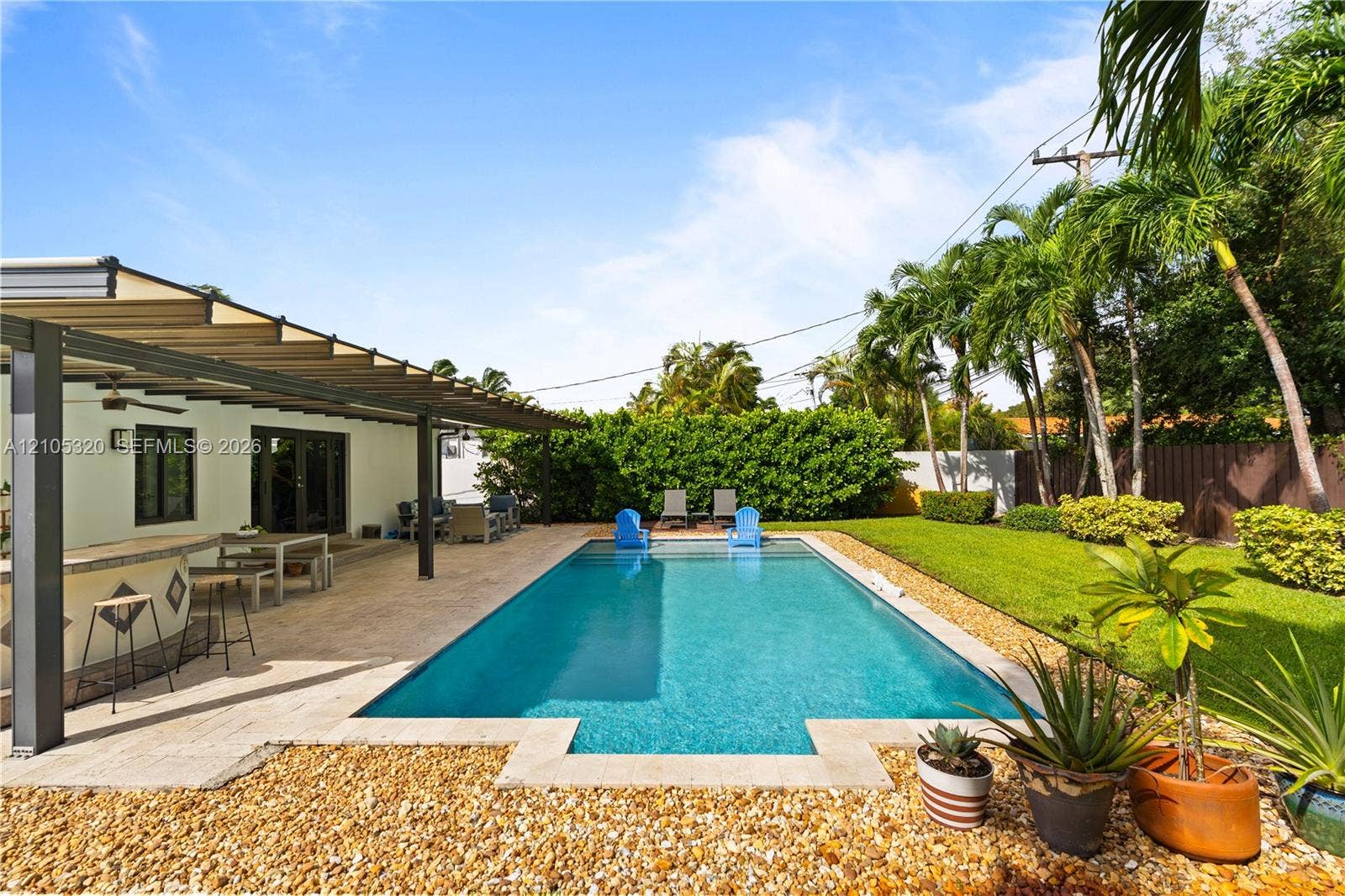 Expansive outdoor living area featuring a rectangular swimming pool, stone paver patio, and covered pergola