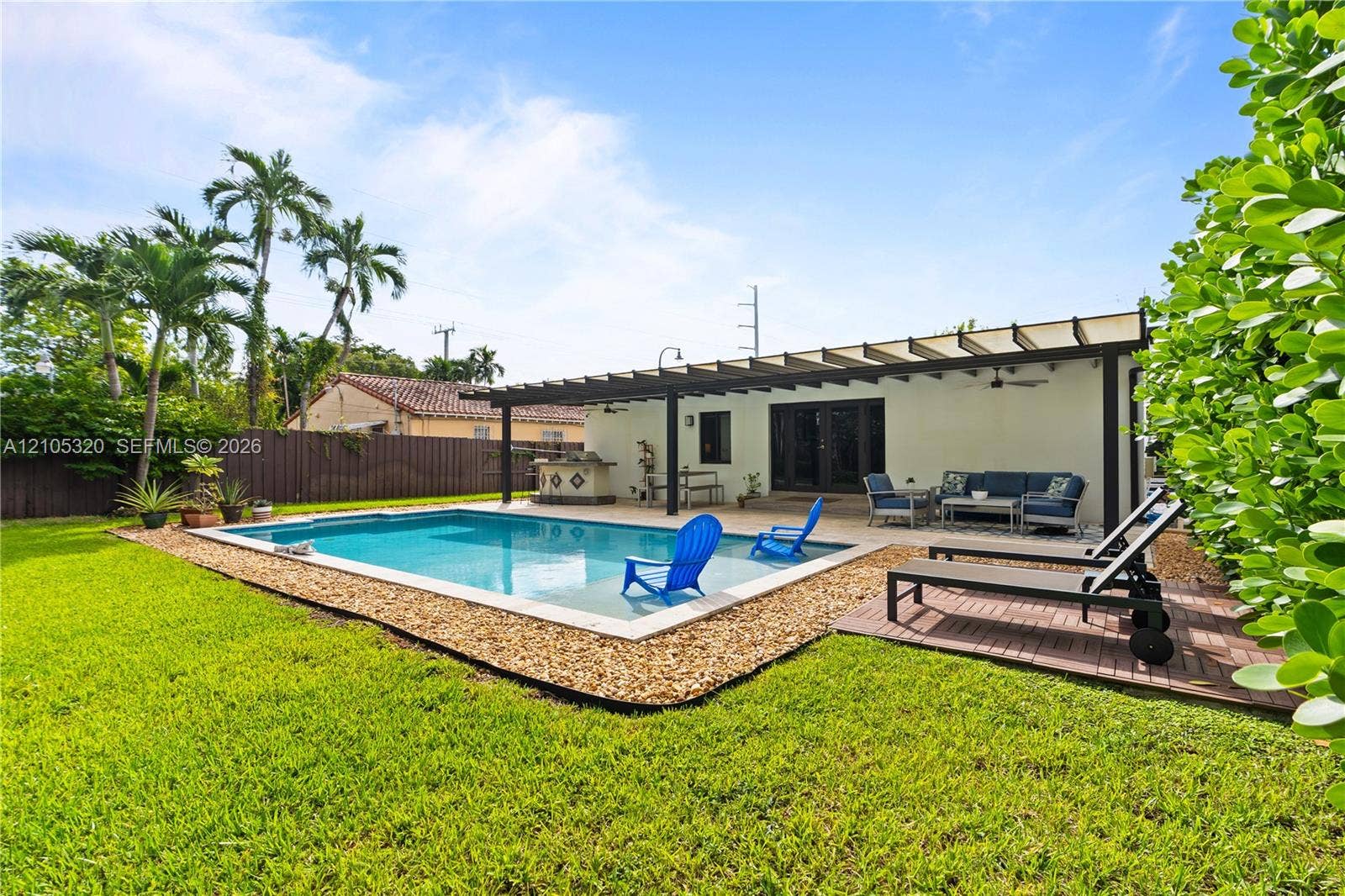 Expansive backyard featuring a rectangular swimming pool, an attached pergola, a built-in outdoor kitchen, a paved patio, and a manicured lawn