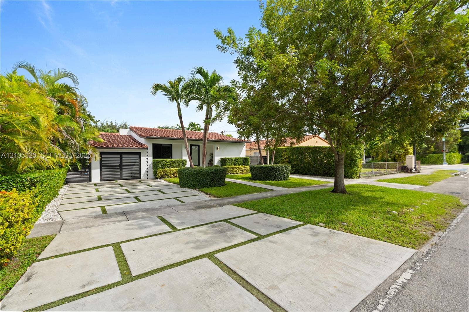 White stucco exterior with a red tile roof, featuring a modern garage door, a patterned concrete driveway, and mature landscaping
