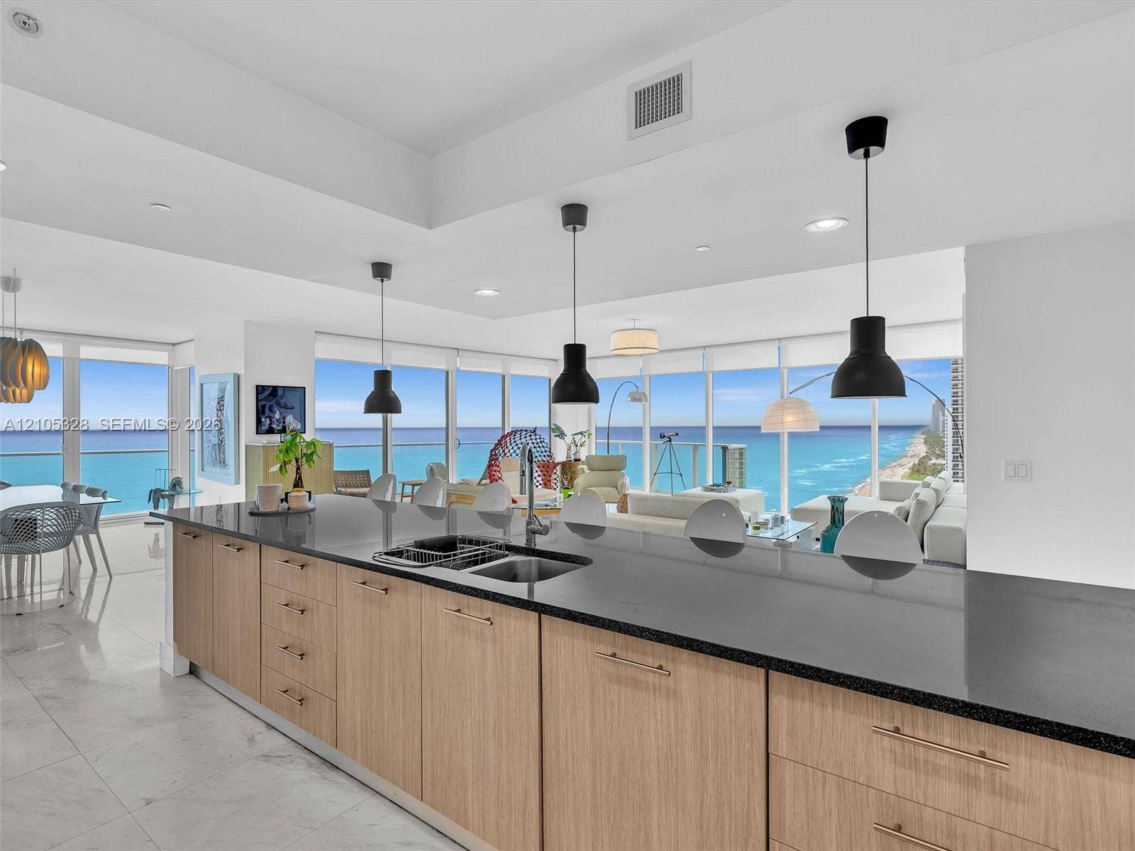 3951 S Ocean Drive, #1901, Hollywood, FL 33019 Modern kitchen featuring a spacious center island with a double sink, sleek black countertops, and elegant wood-finish cabinetry.