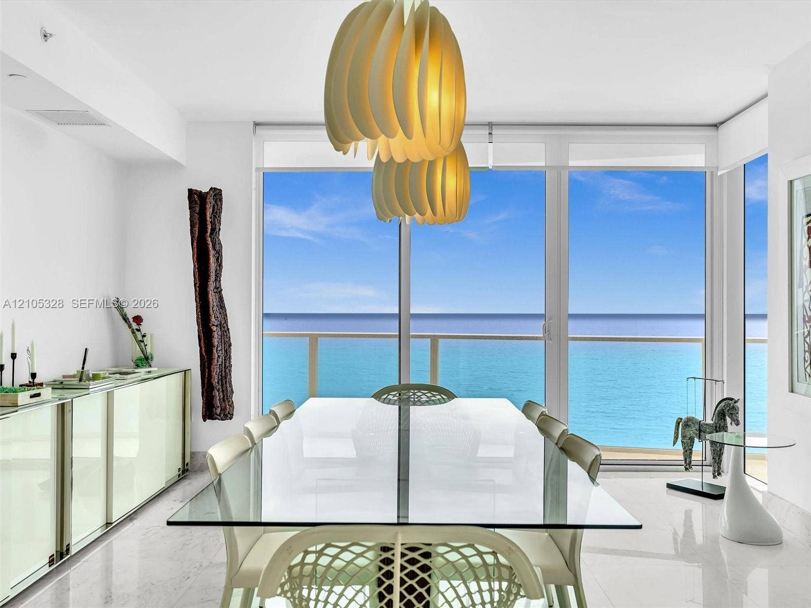 3951 S Ocean Drive, #1901, Hollywood, FL 33019 Elegant dining area featuring floor-to-ceiling glass doors and windows, large-format tile flooring, contemporary pendant lighting, and a glass-top dining table.