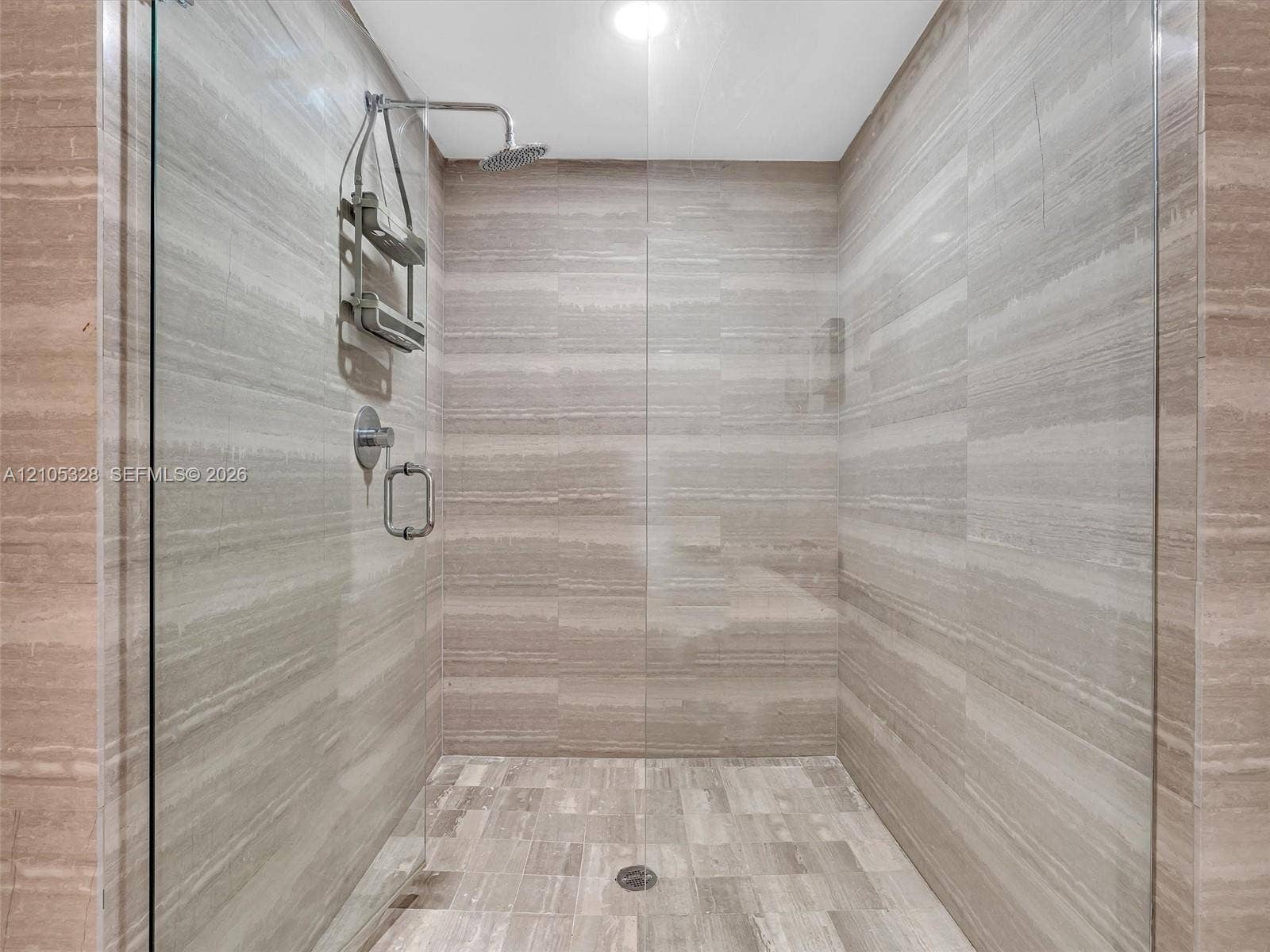 3951 S Ocean Drive, #1901, Hollywood, FL 33019 Luxurious spa-inspired shower featuring a frameless glass enclosure, ceiling-mounted rainfall showerhead, handheld shower, and elegant horizontally patterned wall tiles.