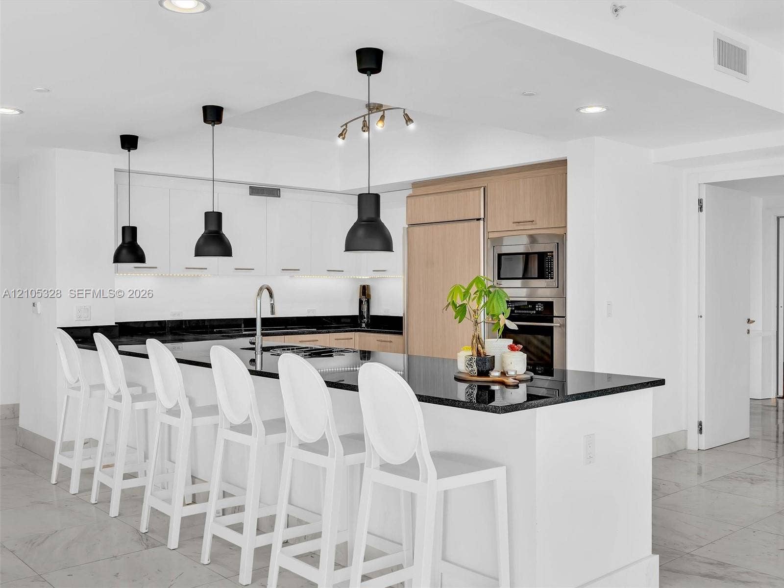3951 S Ocean Drive, #1901, Hollywood, FL 33019 Modern gourmet kitchen featuring an oversized center island with seating, sleek dark stone countertops, stainless steel appliances, and wood-finish cabinetry.