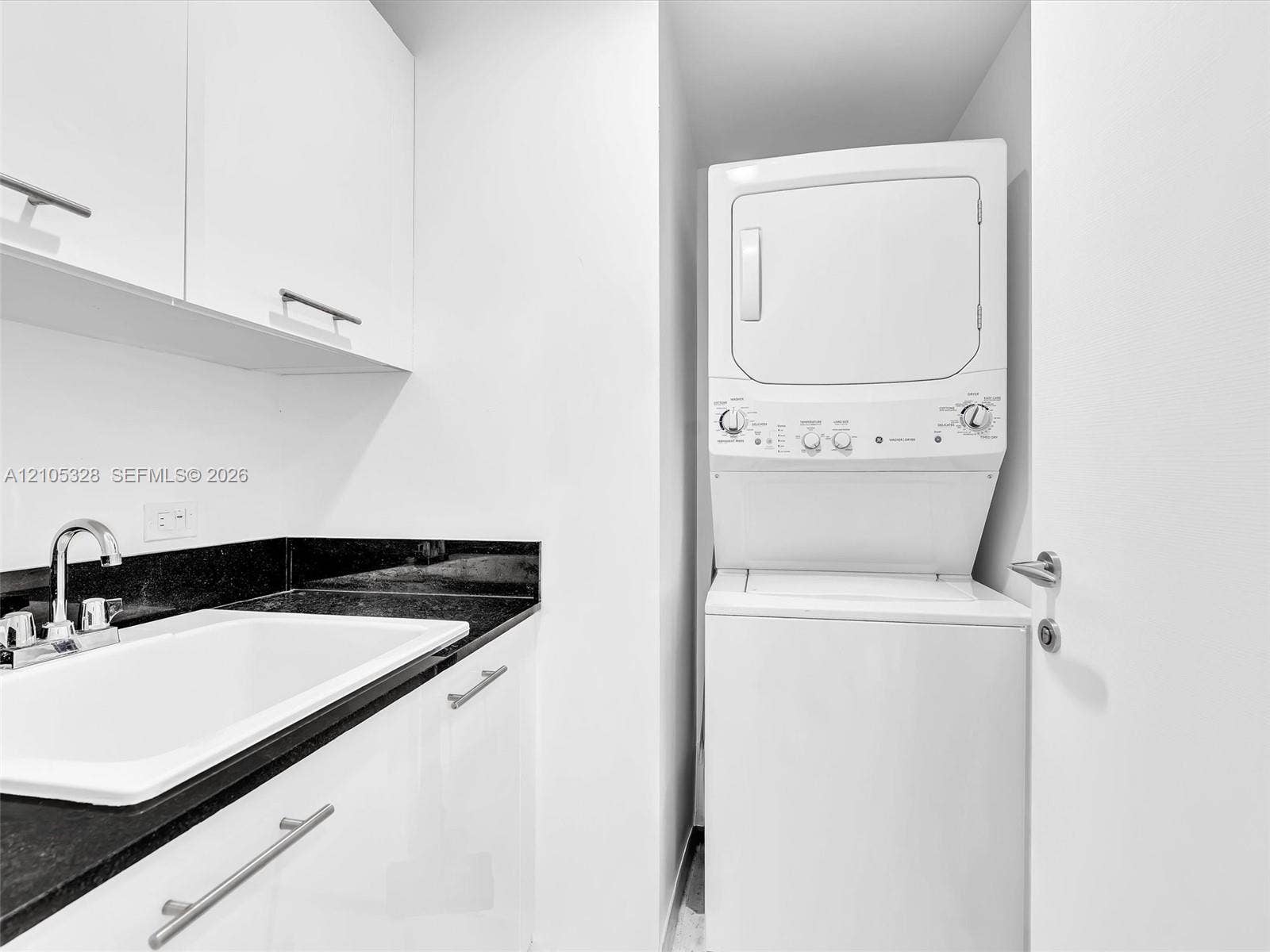 3951 S Ocean Drive, #1901, Hollywood, FL 33019 Stacked washer and dryer unit, white cabinetry with silver-tone pulls, black countertop, and an undermount sink with a chrome faucet