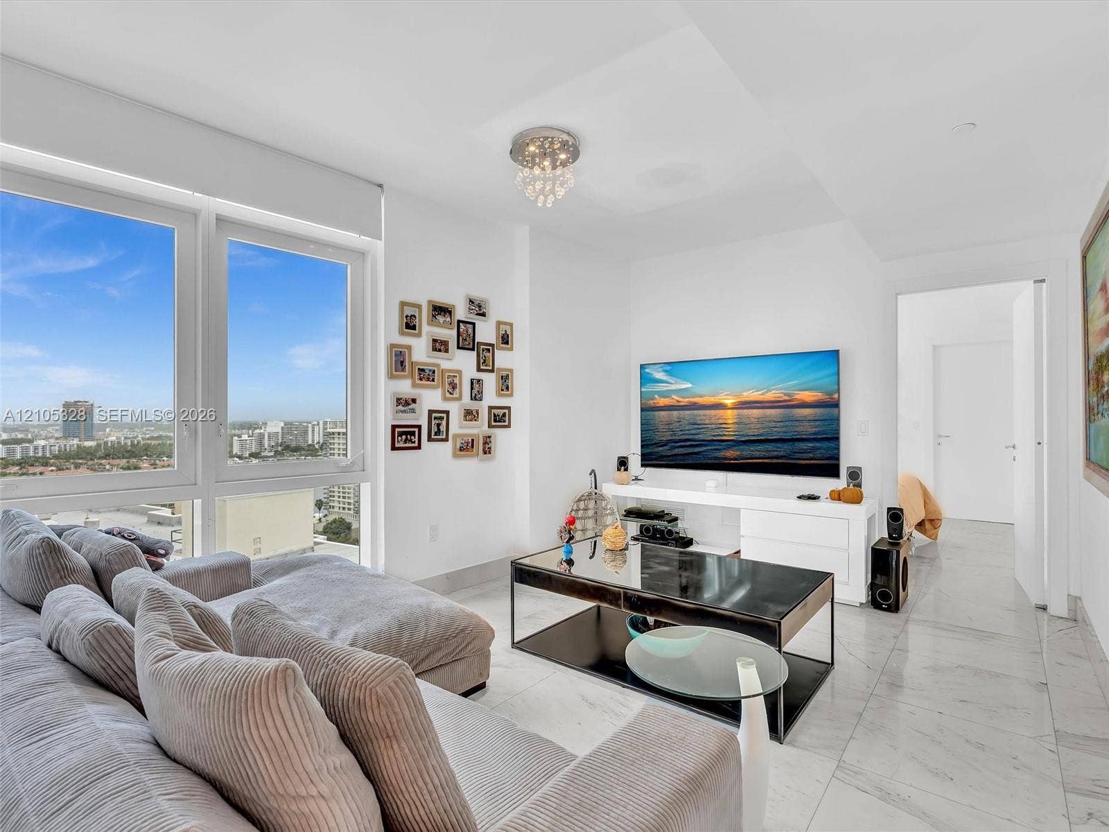 3951 S Ocean Drive, #1901, Hollywood, FL 33019 A luxurious and inviting family room, perfect for relaxing or entertaining, featuring expansive windows with captivating city views, elegant white marble-look flooring, recessed lighting, and a stunning crystal chandelier