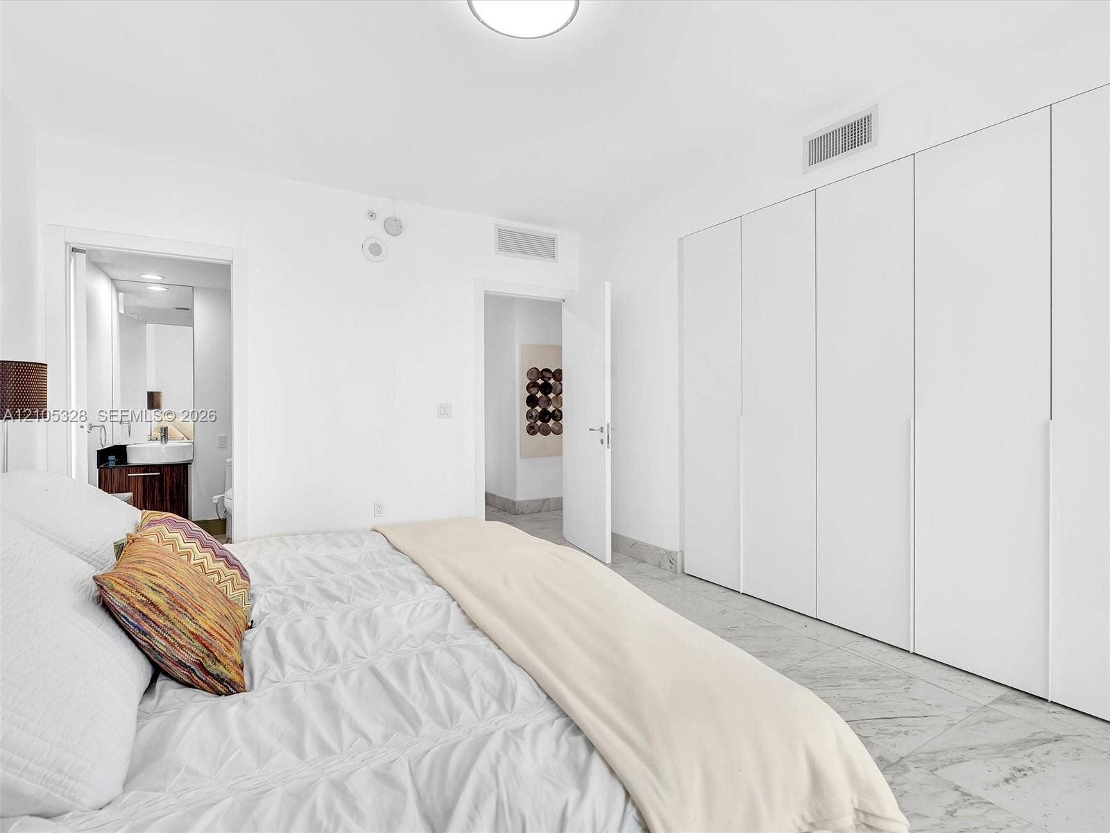 3951 S Ocean Drive, #1901, Hollywood, FL 33019 Bright and elegant bedroom featuring dramatic floor-to-ceiling windows, custom built-in wardrobe cabinetry, luxurious marble-look flooring, recessed ceiling lighting, and a sophisticated white color palette.