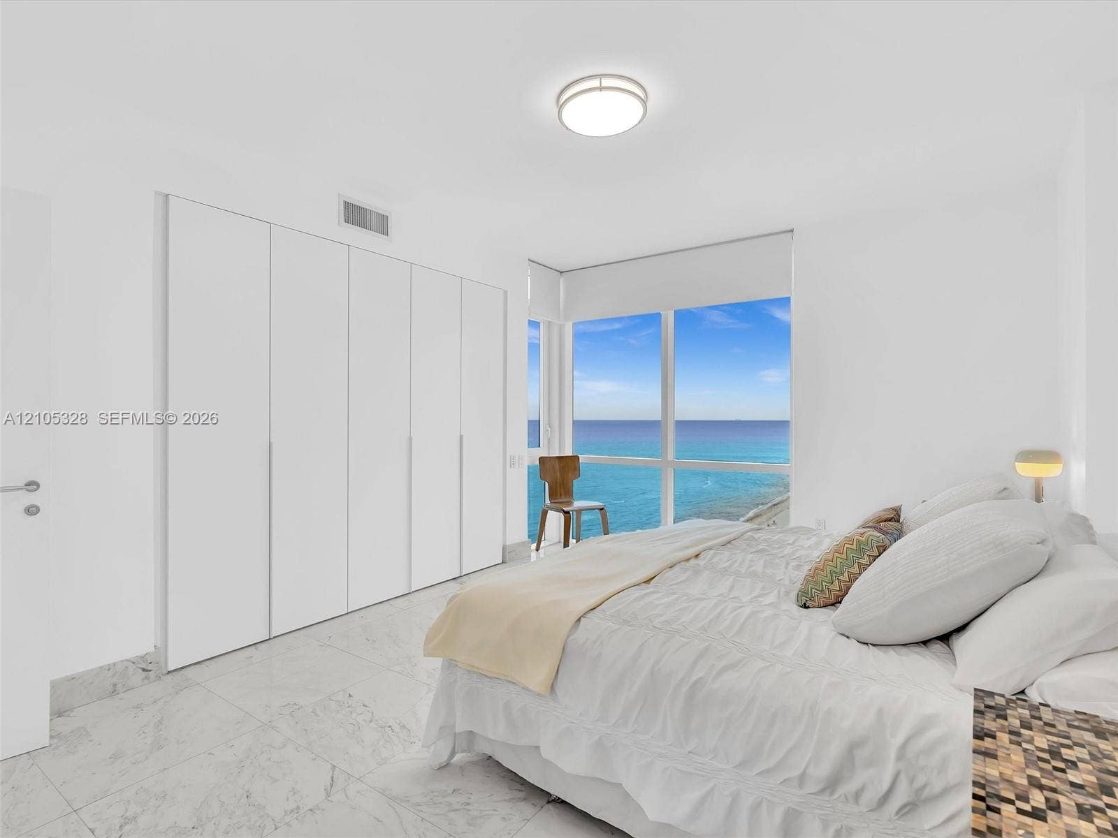 3951 S Ocean Drive, #1901, Hollywood, FL 33019 Bright and elegant bedroom featuring dramatic floor-to-ceiling windows, custom built-in wardrobe cabinetry, luxurious marble-look flooring, recessed ceiling lighting, and a sophisticated white color palette.