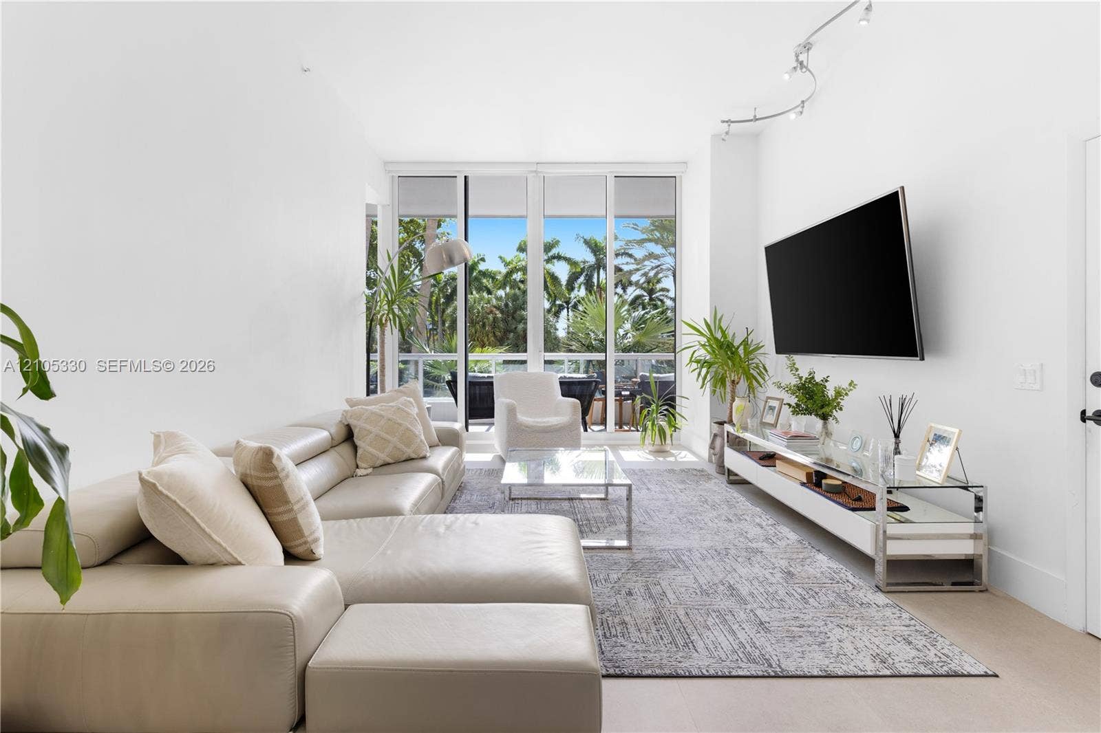 21205 Yacht Club Drive, #304, Aventura, FL 33180 Bright, light-filled living space showcasing floor-to-ceiling glass doors opening to outdoor grounds, neutral wood-finish flooring, and a neutral-toned sectional arrangement
