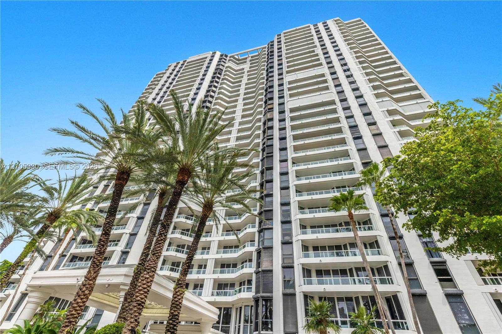 21205 Yacht Club Drive, #304, Aventura, FL 33180 High-rise structure featuring multiple private balconies, a grand entrance with a porte-cochre, and surrounding palm trees