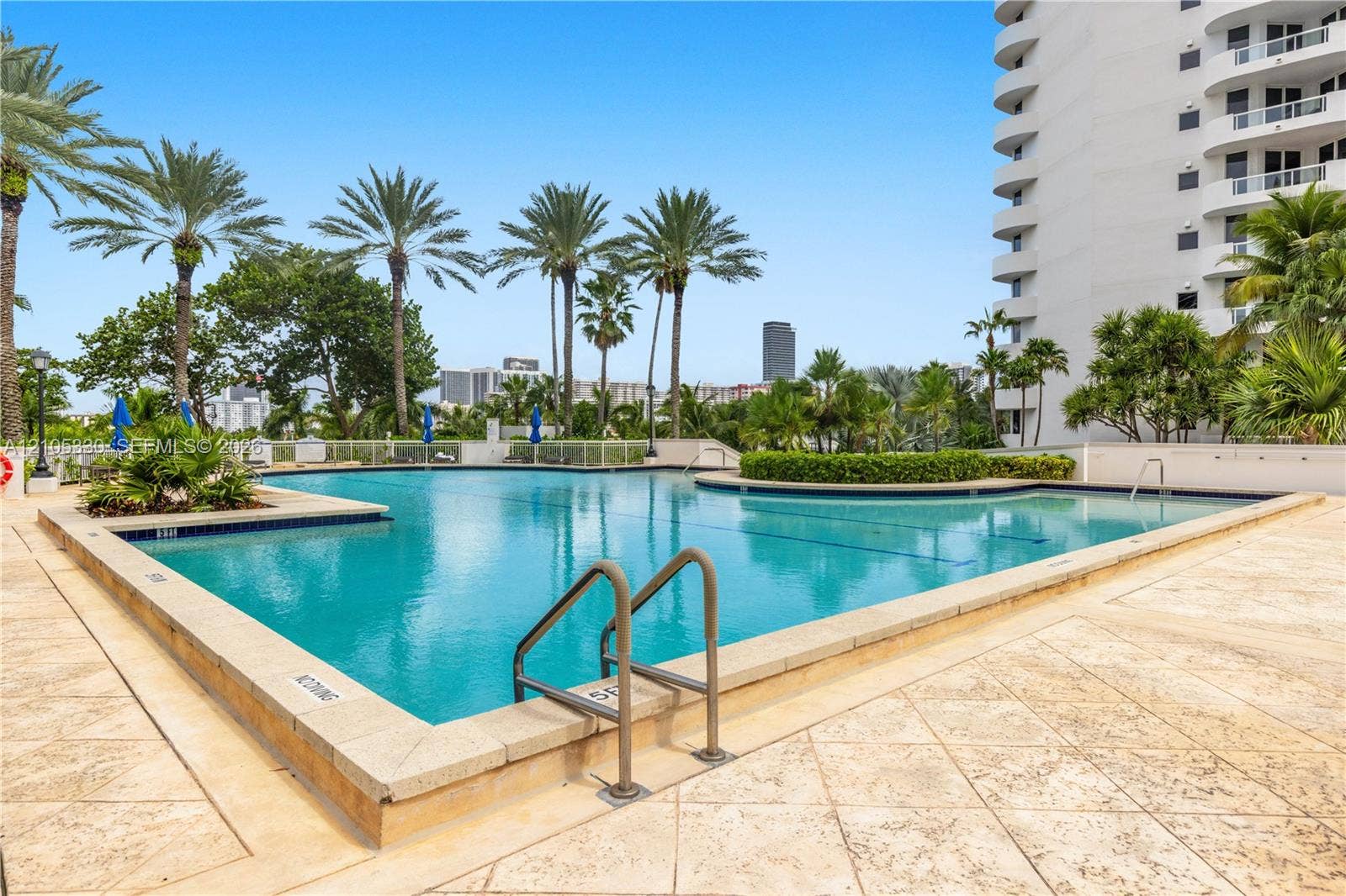 21205 Yacht Club Drive, #304, Aventura, FL 33180 Expansive outdoor pool with integrated shallow section, surrounded by textured paving, lush landscaping, and mature palm trees