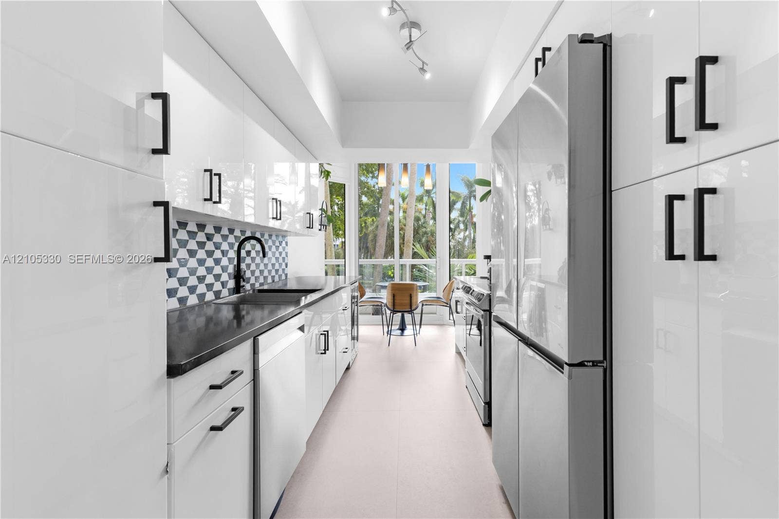 21205 Yacht Club Drive, #304, Aventura, FL 33180 Galley kitchen featuring white cabinetry, black countertops, a geometric tile backsplash, stainless steel appliances, and track lighting