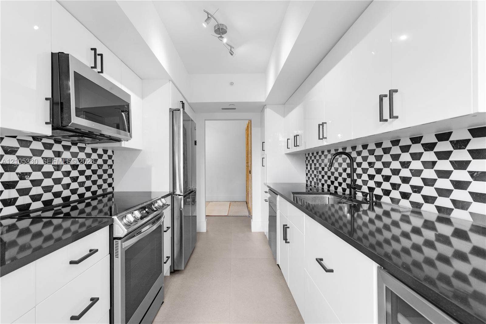 21205 Yacht Club Drive, #304, Aventura, FL 33180 Galley kitchen featuring white cabinetry, stainless steel appliances, black countertops, a geometric pattern backsplash, and track lighting