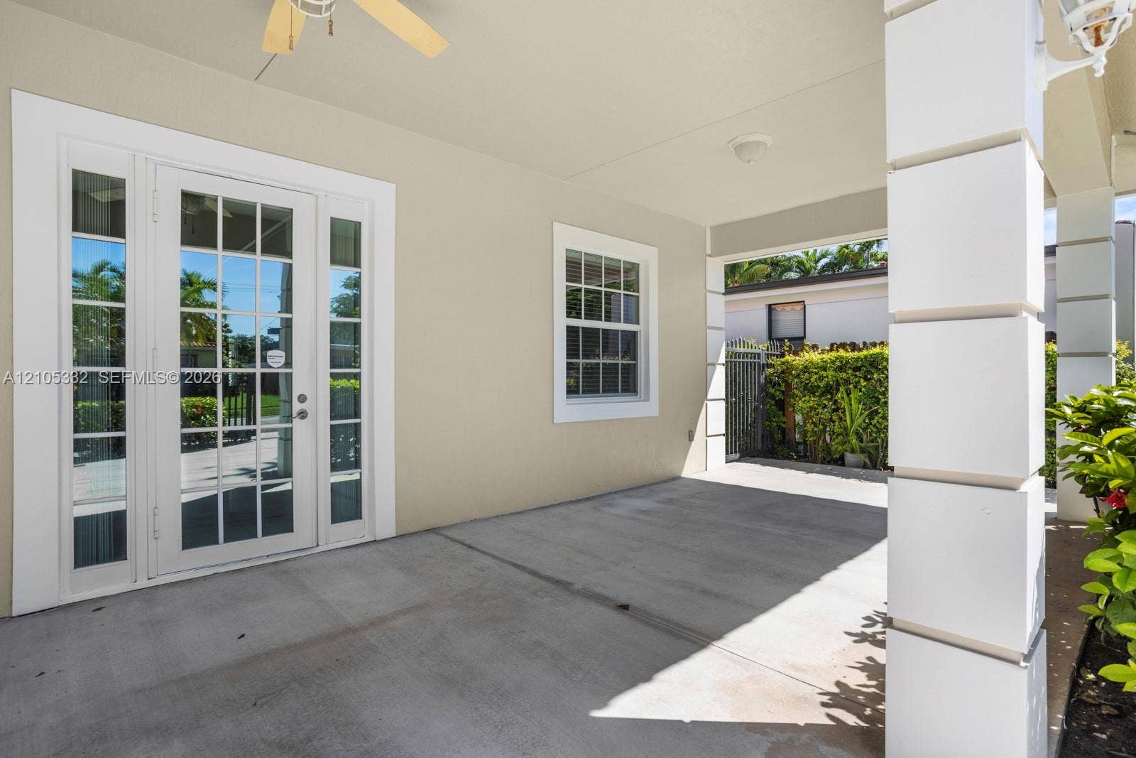Covered patio featuring French doors with sidelights, a window with louvered shutters, a ceiling fan, and decorative support columns