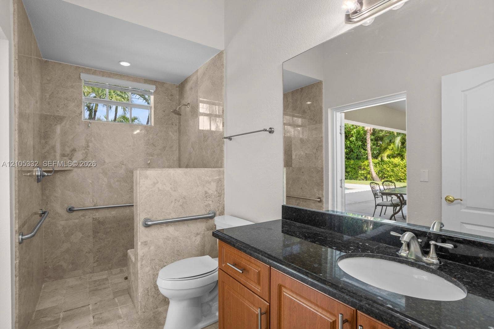 Walk-in shower with tiled walls and flooring, vanity with dark stone countertop, single basin sink, and wood-finish cabinetry