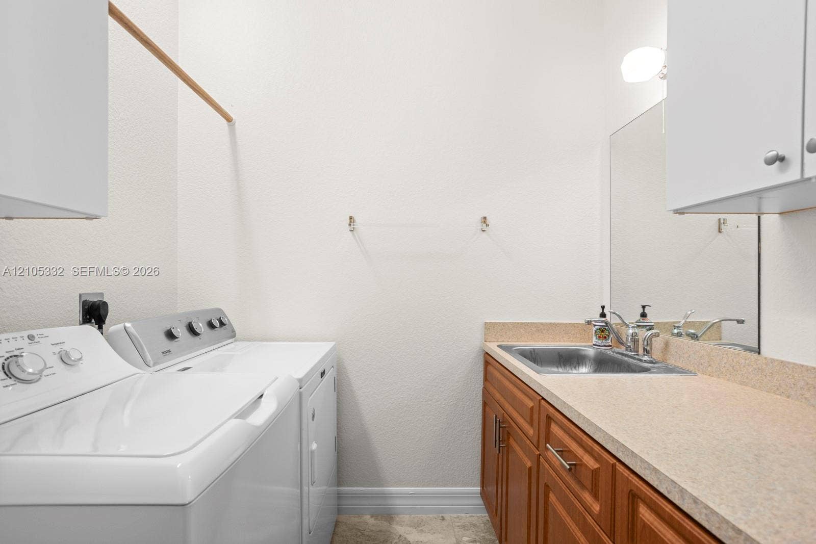 Laundry area with light-toned countertop, wood-finish cabinetry, and a stainless steel utility sink